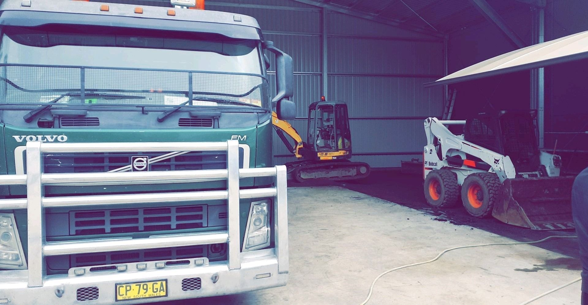 A volvo truck is parked in a garage next to a bobcat excavator.