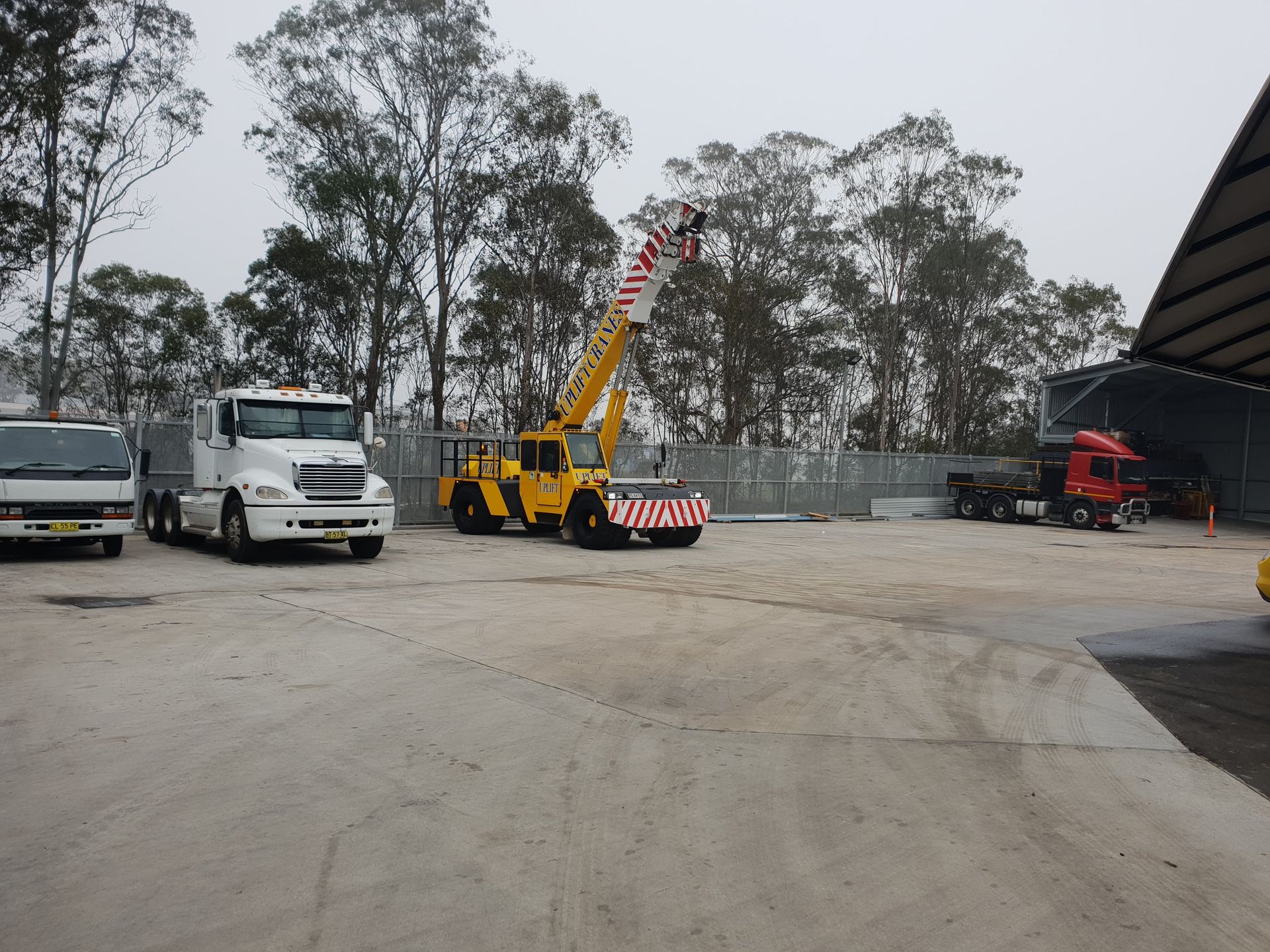 A yellow crane is parked next to a white truck