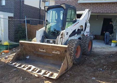 A bobcat skid steer loader is parked in front of a brick building.