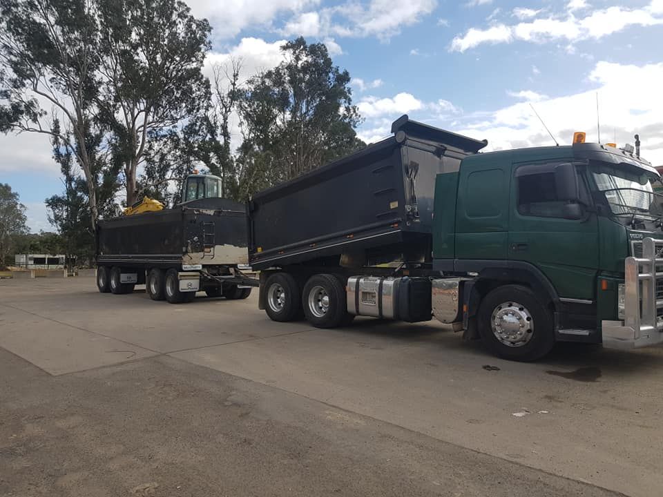A green dump truck is parked next to a black dump truck.
