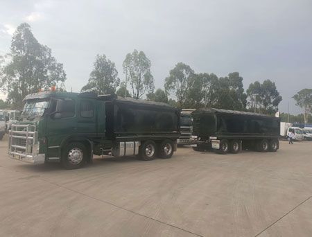 A green truck with a trailer attached to it is parked in a parking lot.