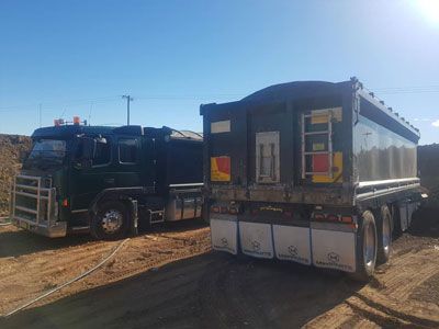 Two dump trucks are parked next to each other on a dirt road.