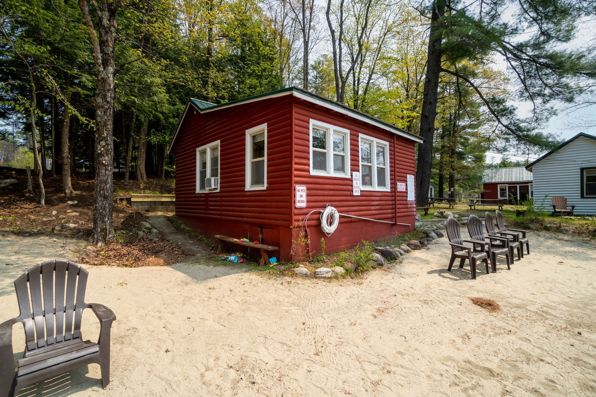 Red lakeside cabin with white-framed windows; beach chairs on sand.