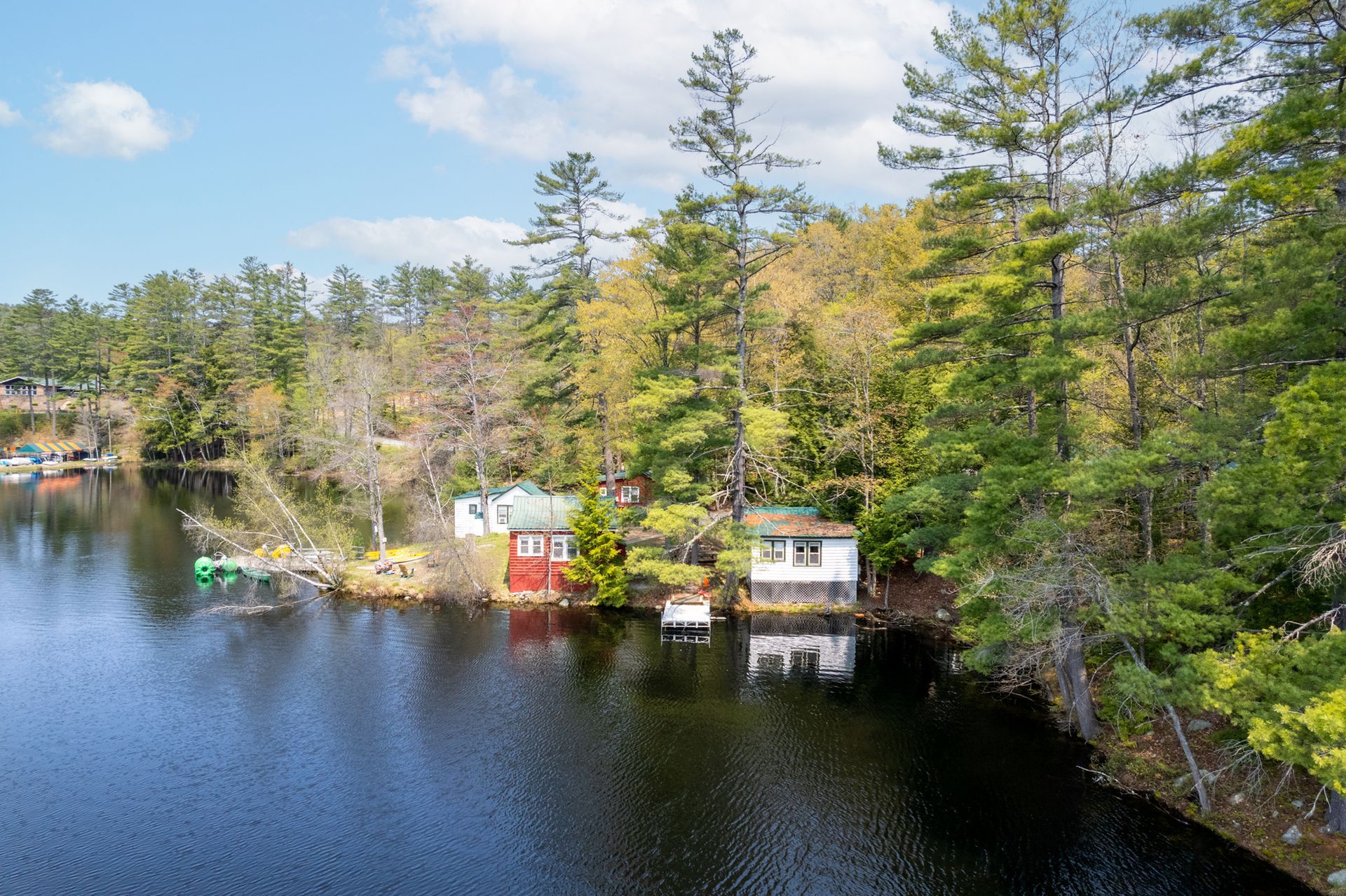 Lakeside view of two small cabins nestled among trees with dark water in the foreground and a blue sky above.