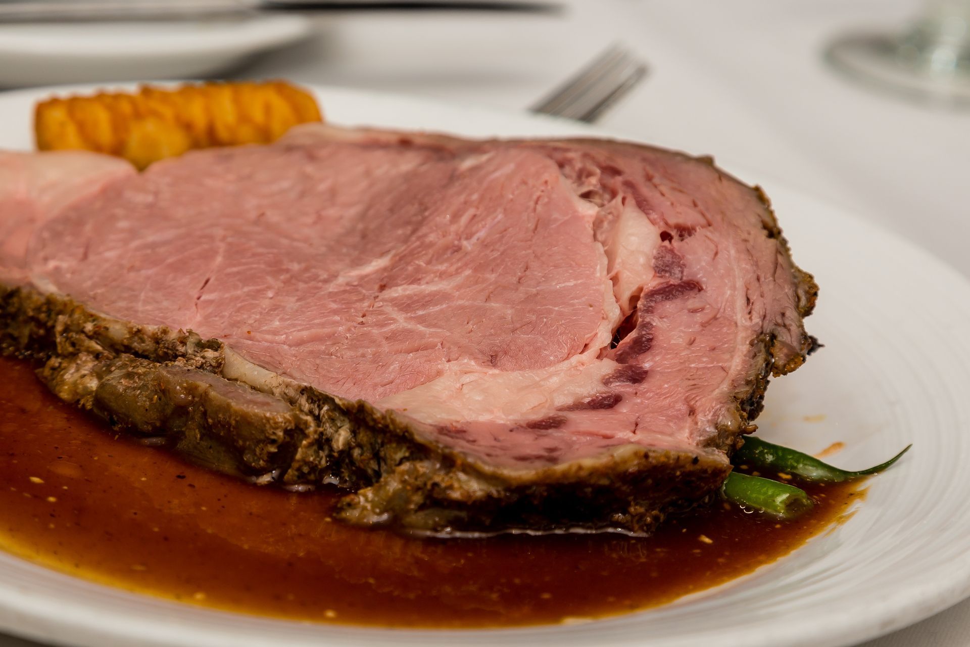 Sliced prime rib with gravy and asparagus on a white plate.