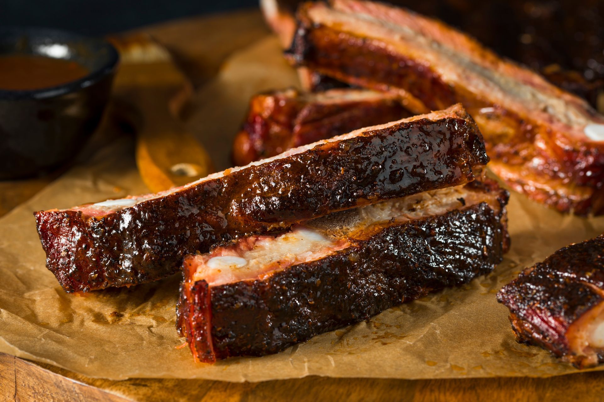 Smoked barbecue ribs on parchment paper, with a small bowl of sauce.