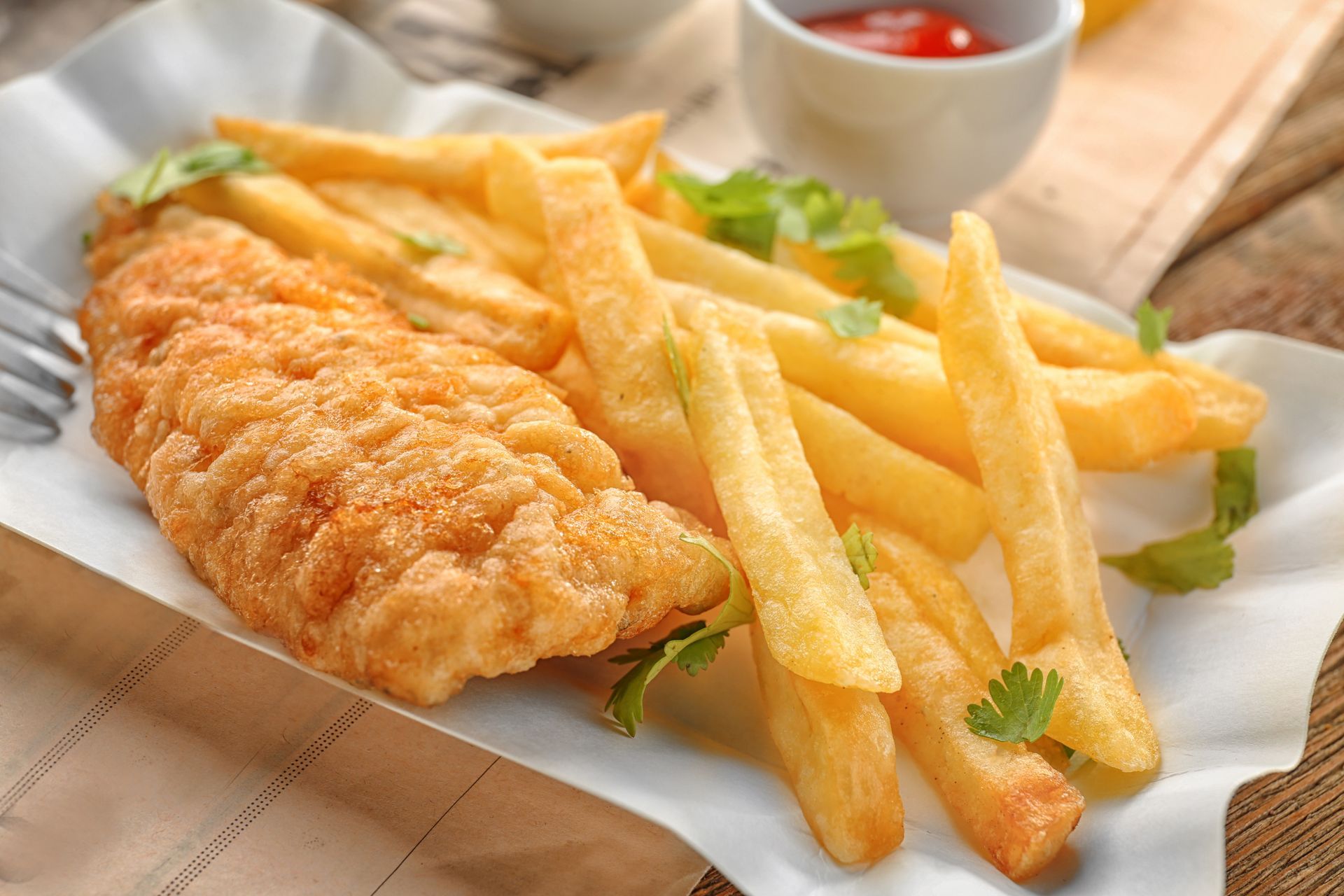 Fish and chips on a white paper-lined tray, with ketchup in a small white cup, garnished with parsley.