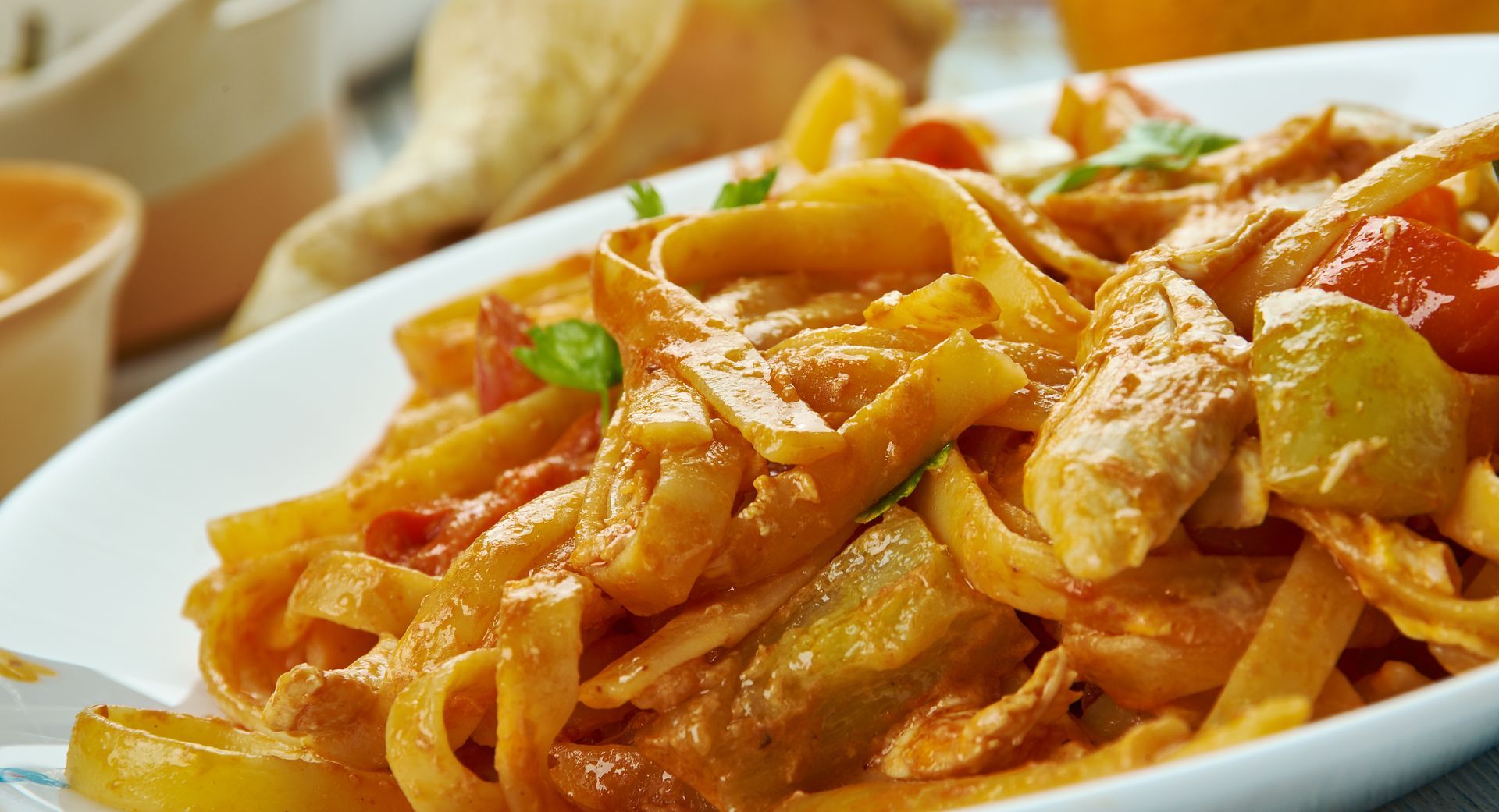 Pasta with creamy orange sauce, vegetables, and chicken, on a white plate.