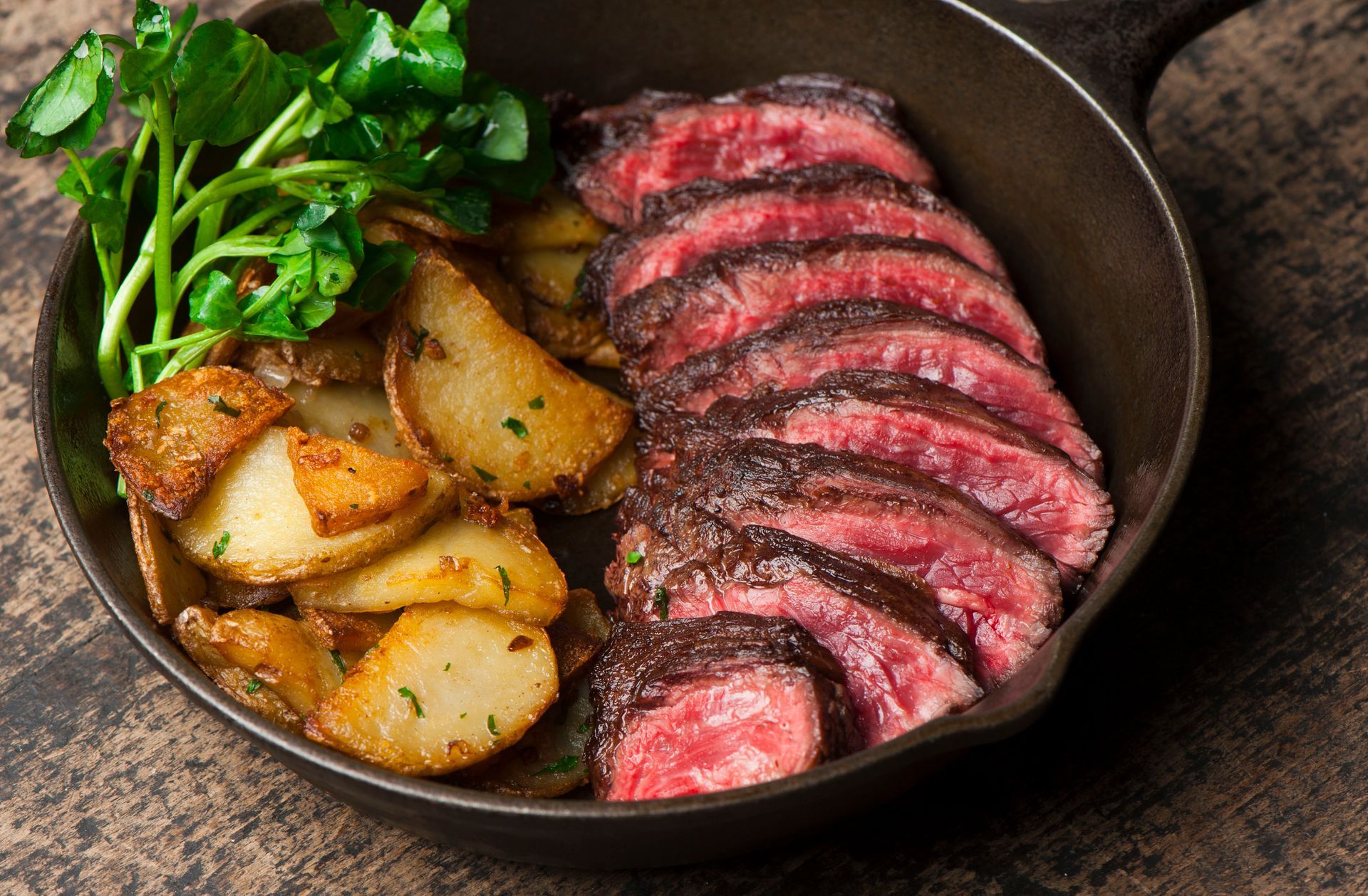 Sliced steak with roasted potatoes and greens in a cast iron skillet.
