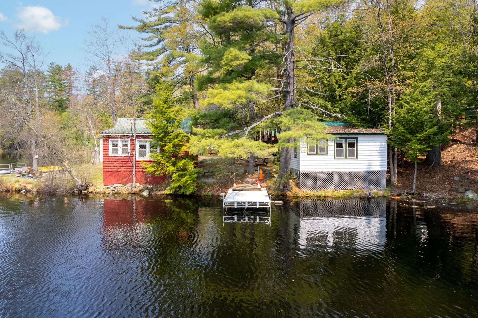 Red and white lakeside cabins reflected in calm water, surrounded by trees.