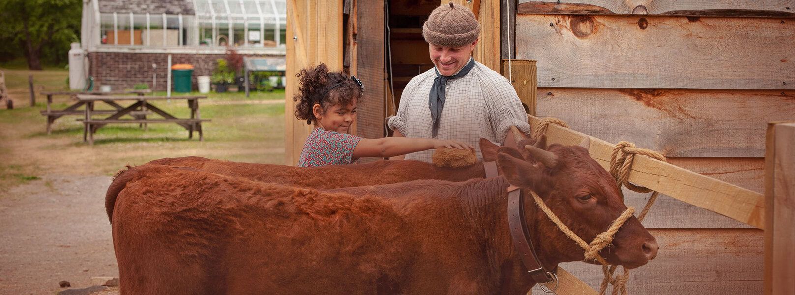 A child and a man petting a brown cow in a barn.