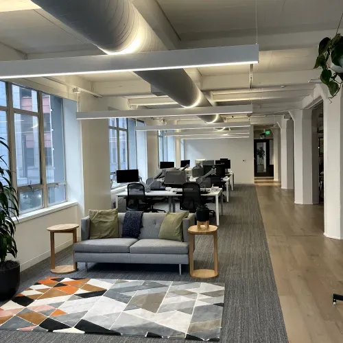 A large office with a couch , tables , chairs and a rug.