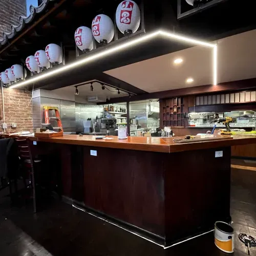 A restaurant with a long wooden counter and lanterns hanging from the ceiling.