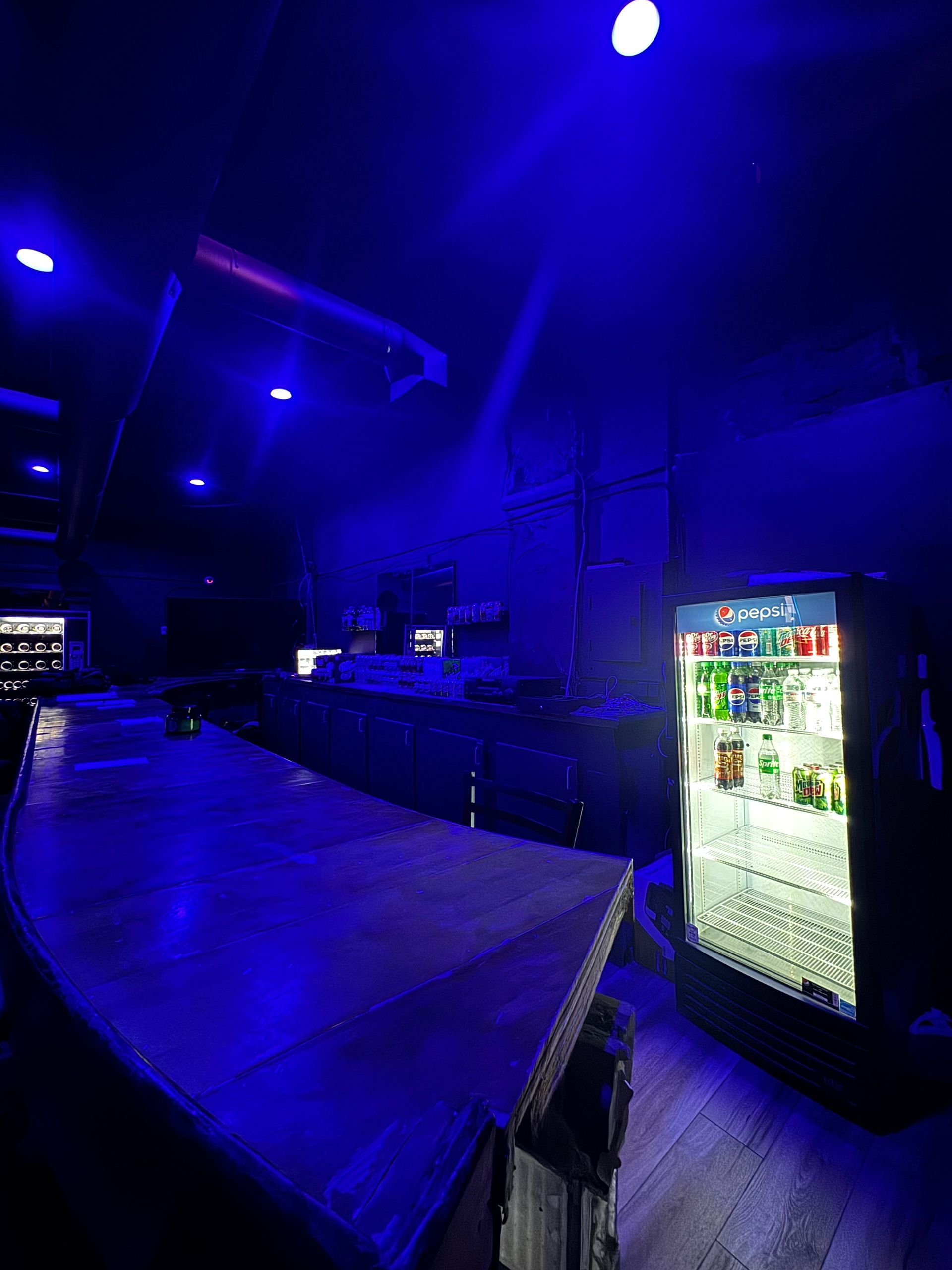 A bar with a refrigerator and a blue light on the ceiling.