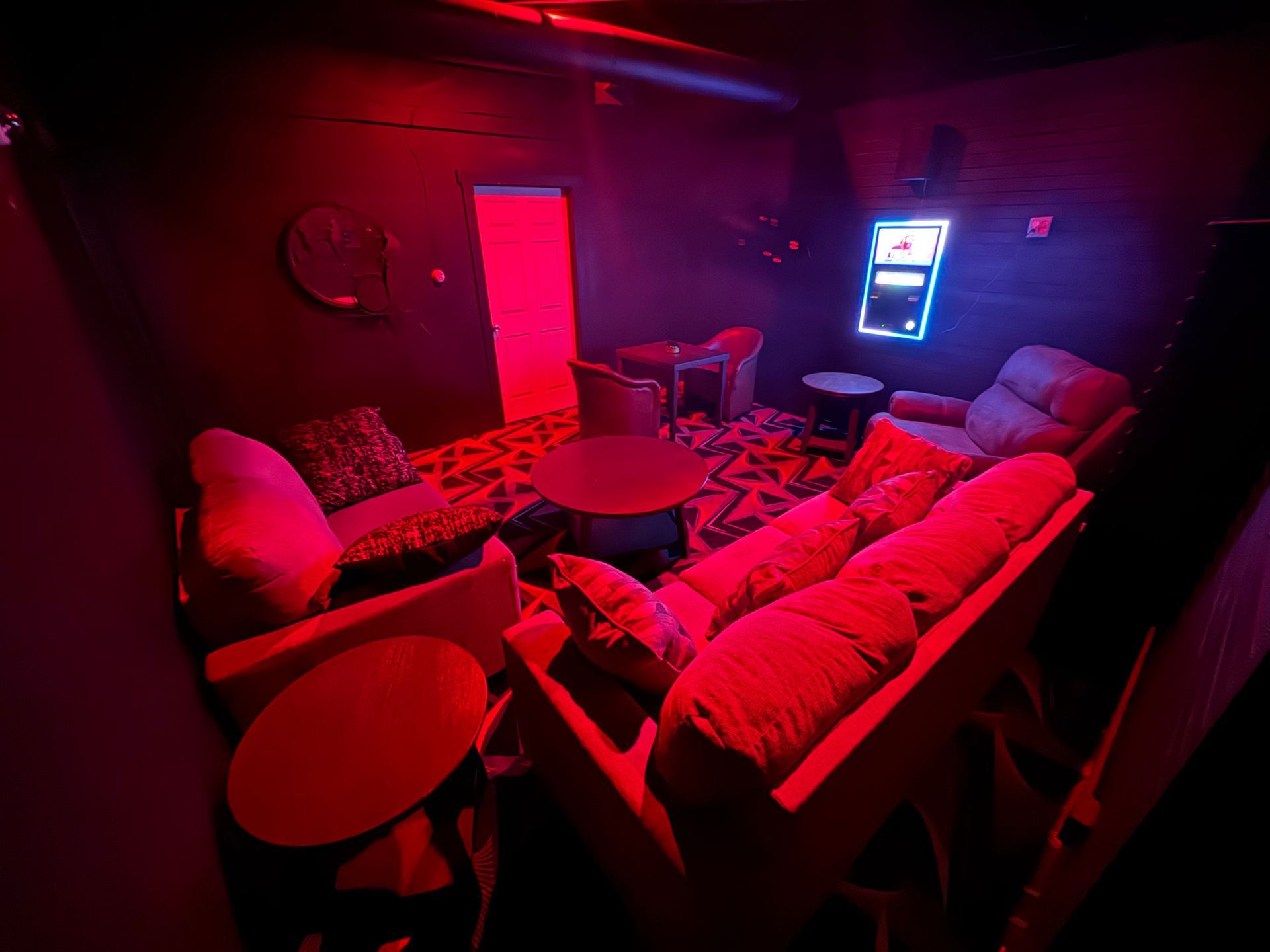 A living room with a couch , chairs , tables and a neon sign.