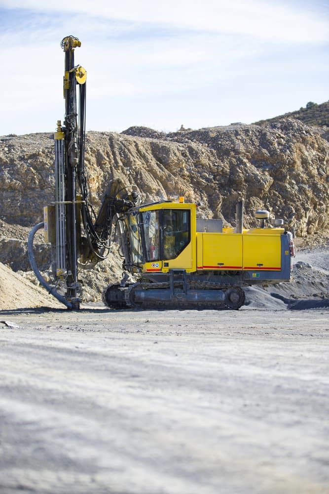 A Yellow Excavator is Driving Through a Dirt Field in a Quarry — FNQ Drilling in Babinda, QLD