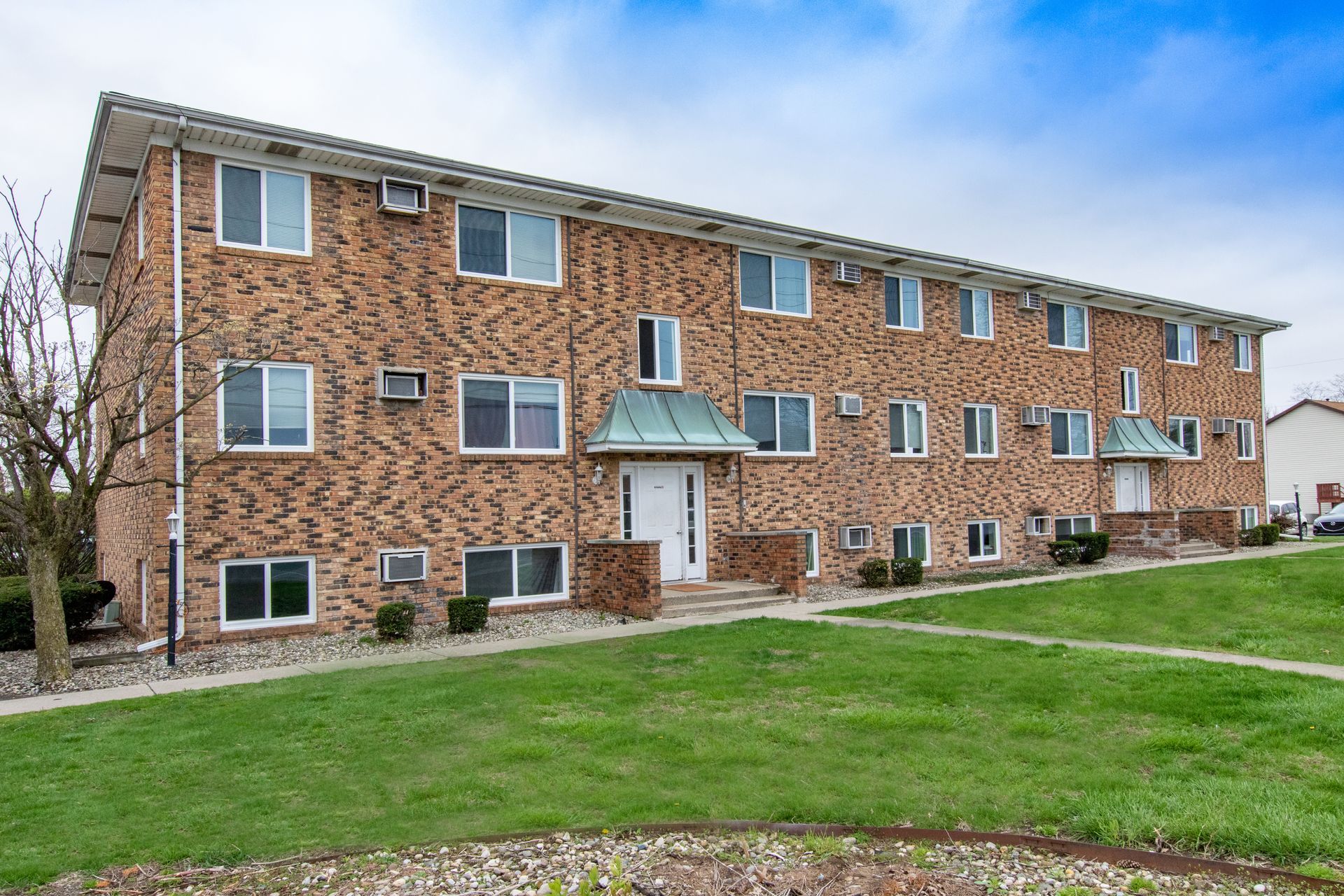 Two-story brick apartment building with white windows and doors, green lawn.