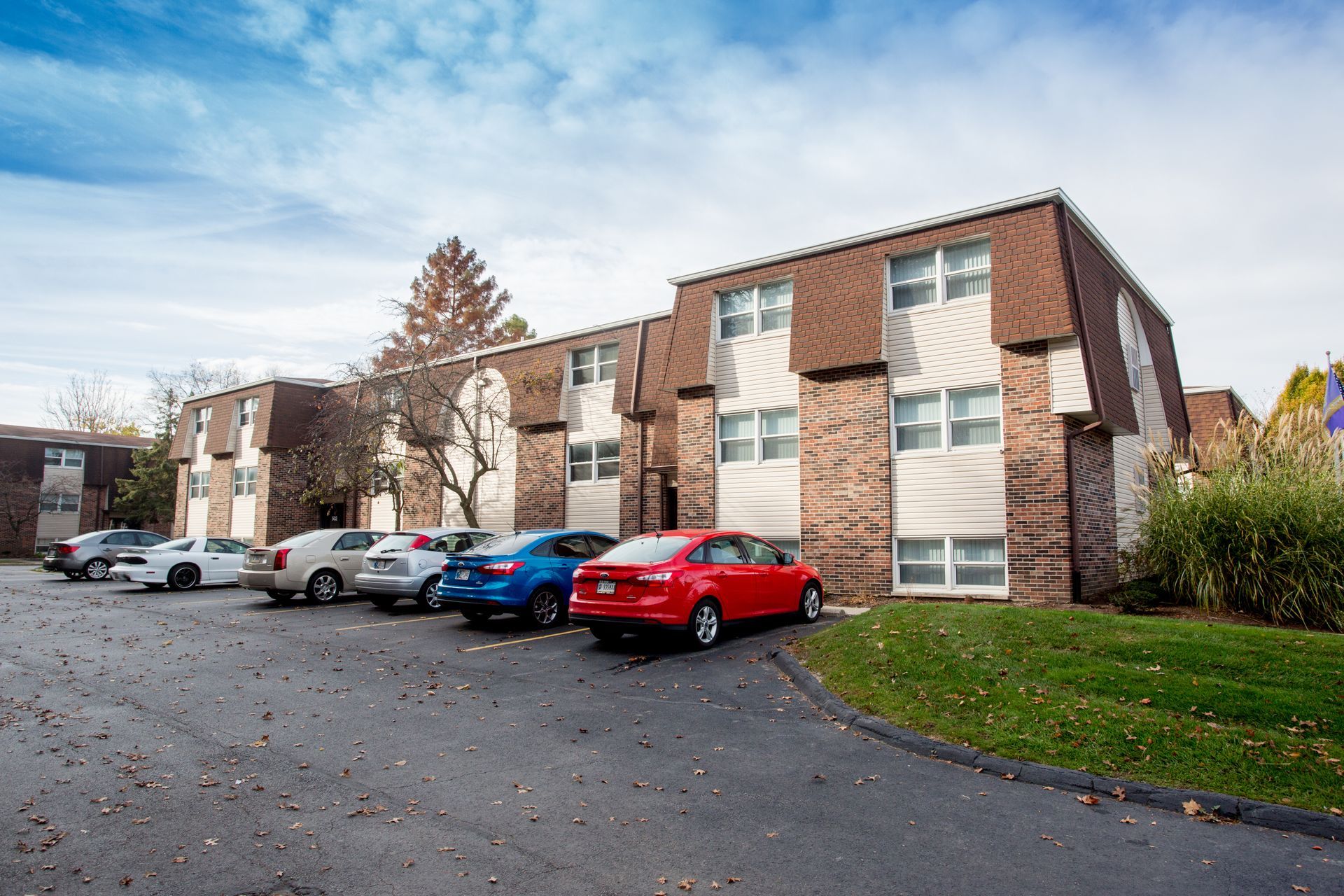 Apartment building with cars parked in front on an asphalt lot; blue sky.