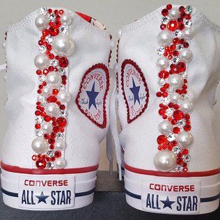 A pair of white converse all star shoes decorated with red rhinestones and pearls
