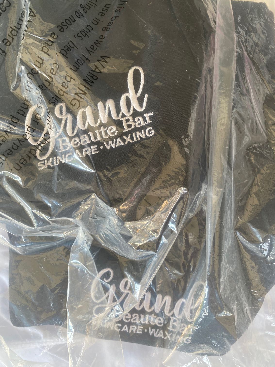 A black plastic bag with the words `` grand beaute bar skincare waxing '' written on it.