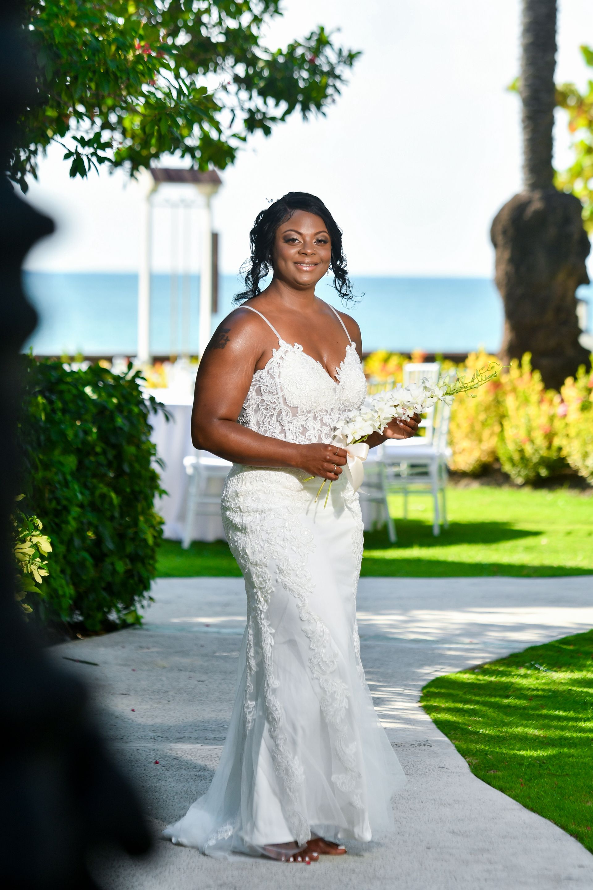 A woman in a white dress is standing on a sidewalk holding a bouquet of flowers.