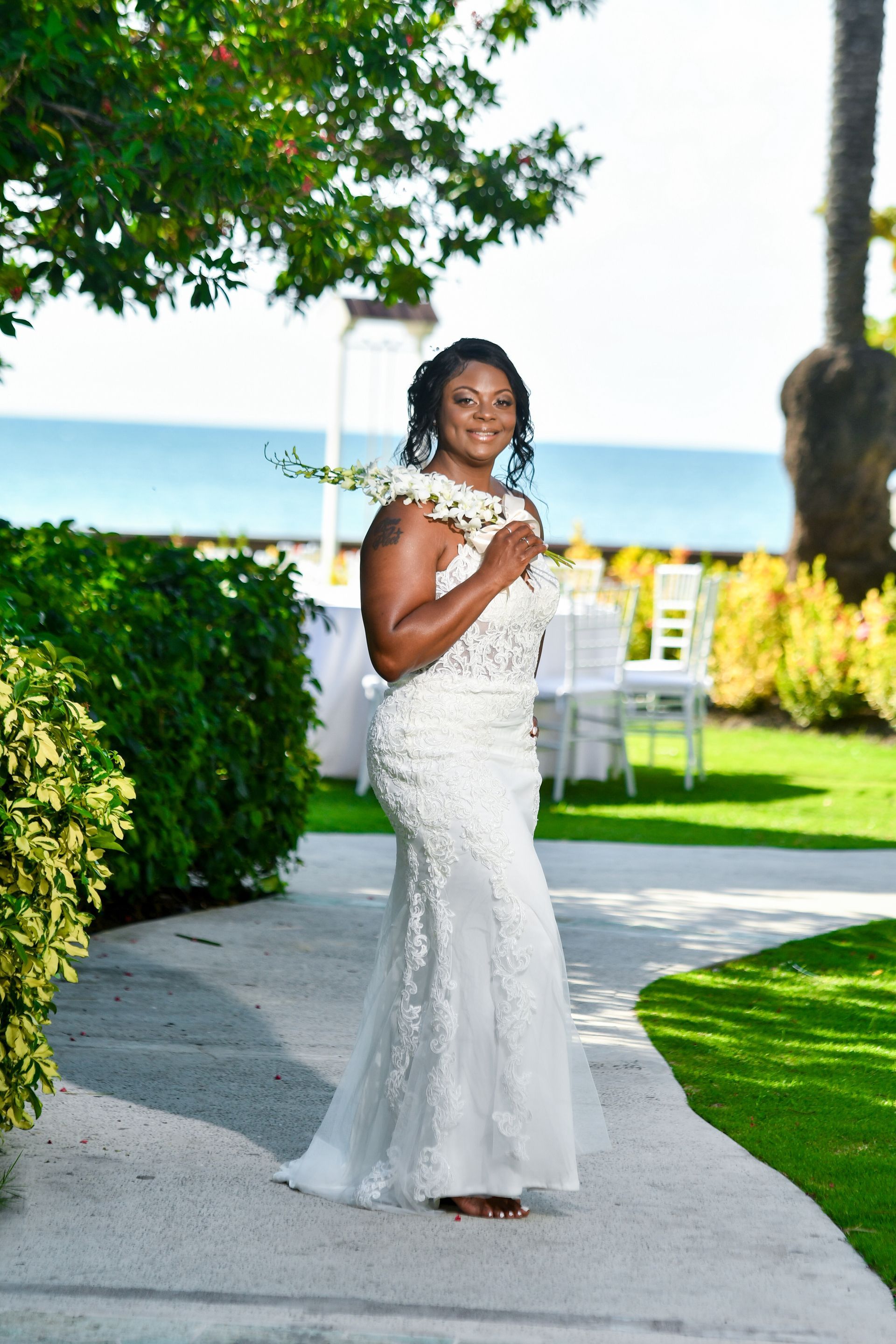 A woman in a white dress is standing on a sidewalk holding flowers.