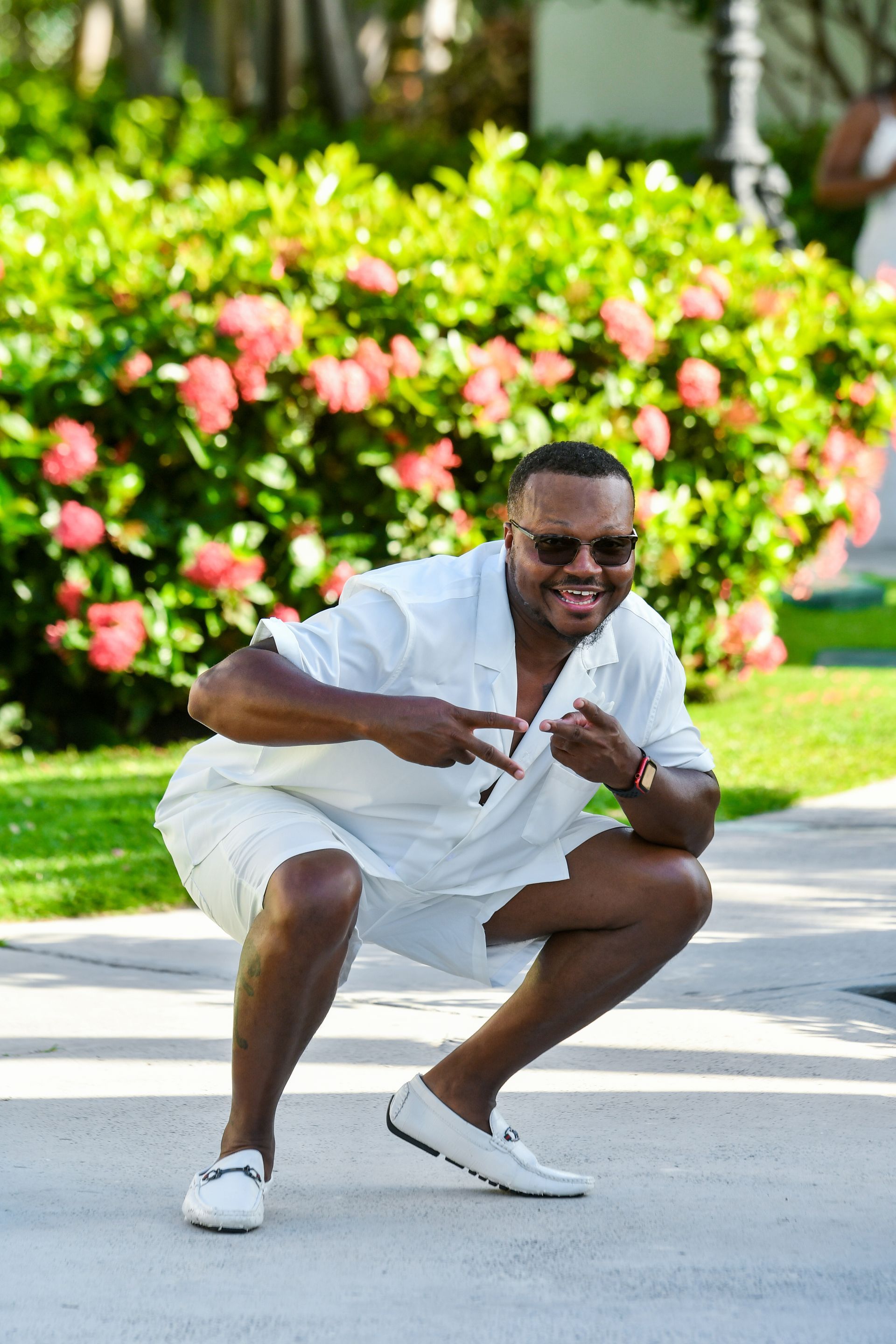 A man in a white shirt and shorts is squatting down and pointing at something.