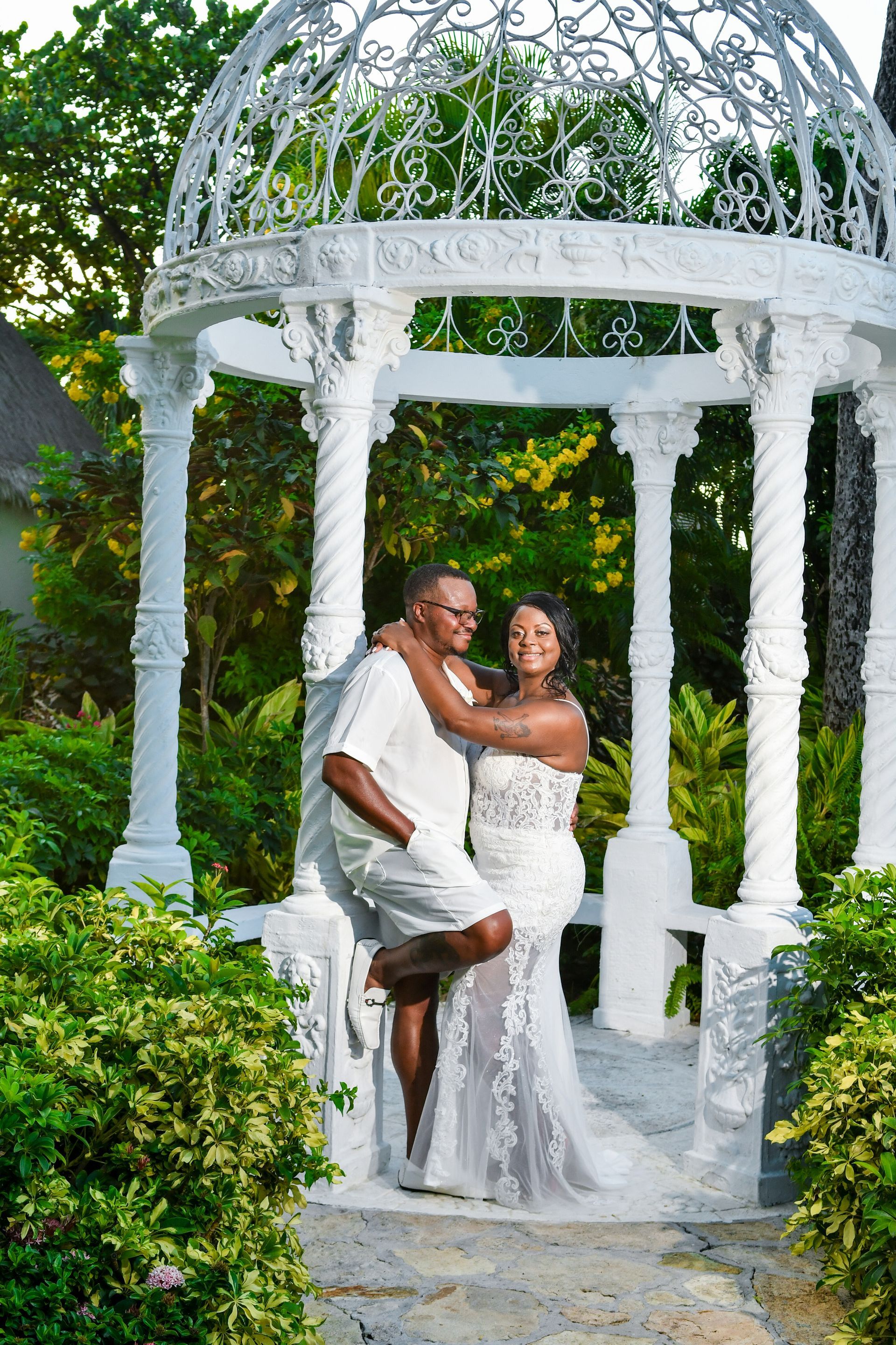 A man is holding a woman in his arms in front of a white gazebo.