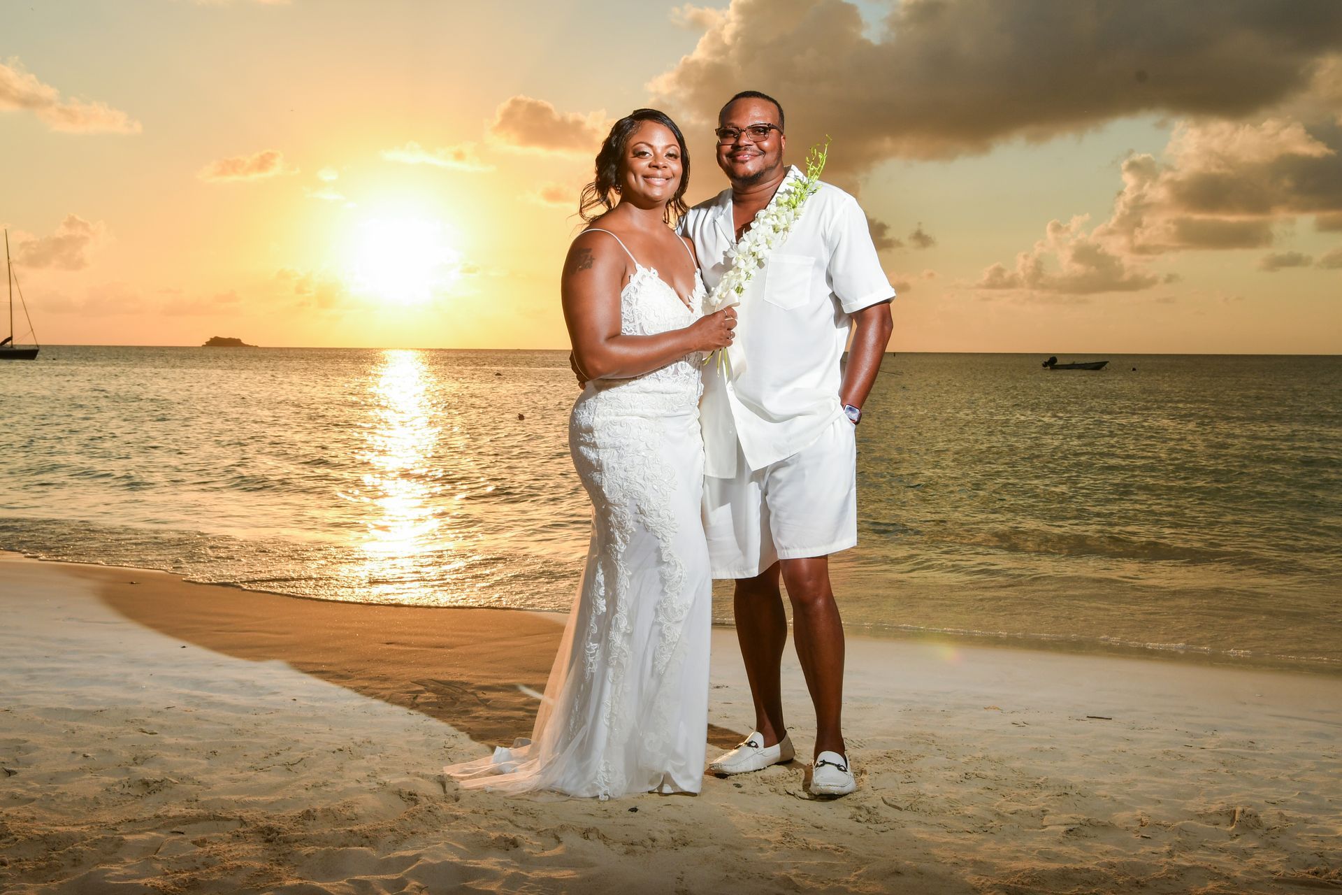 A bride and groom are posing for a picture on the beach at sunset.