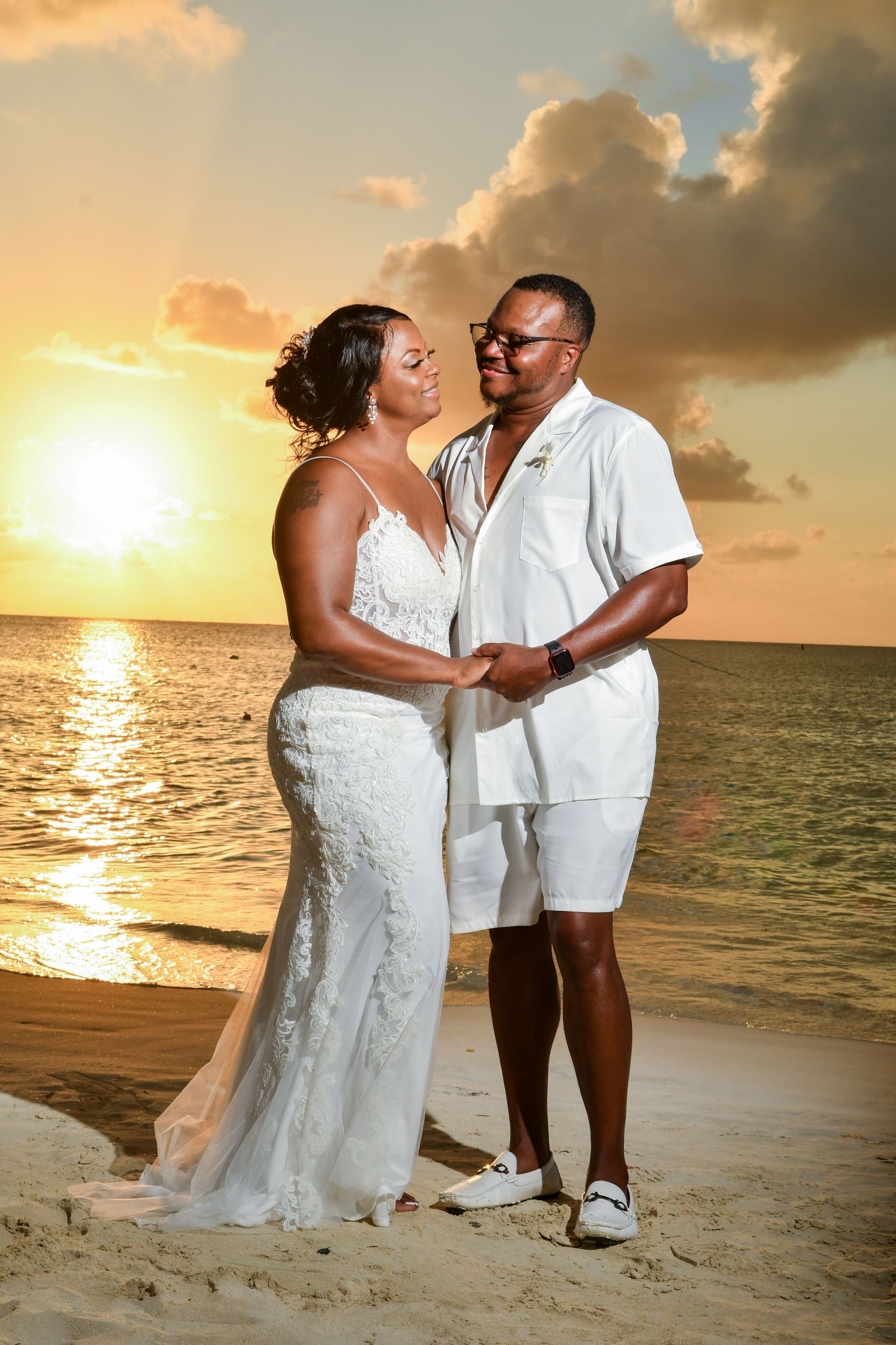 A bride and groom are posing for a picture on the beach at sunset.