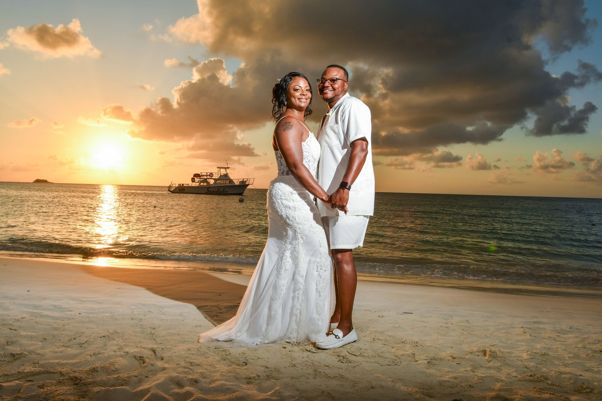 A bride and groom are posing for a picture on the beach at sunset.