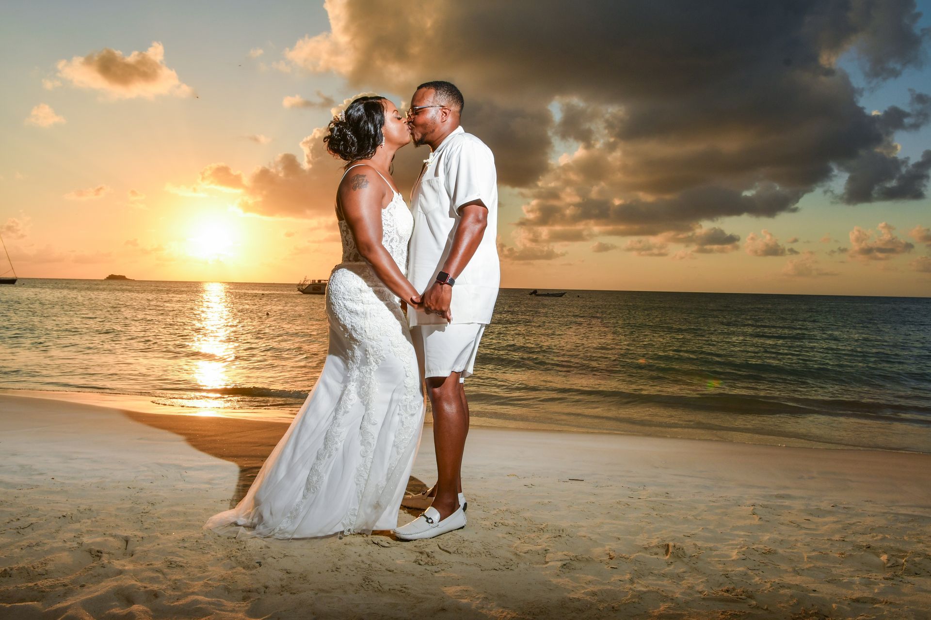A bride and groom are kissing on the beach at sunset.