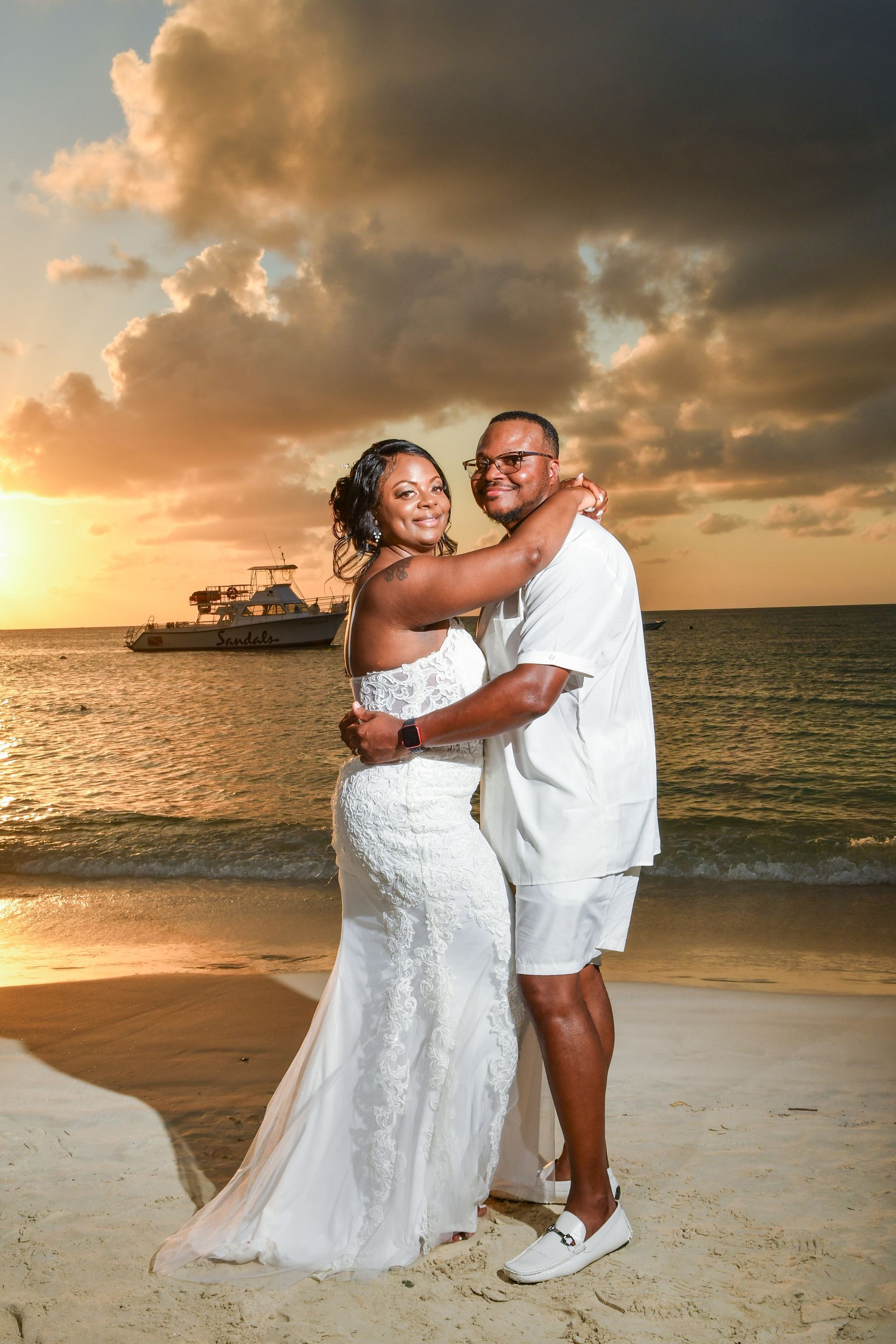 A bride and groom are posing for a picture on the beach at sunset.