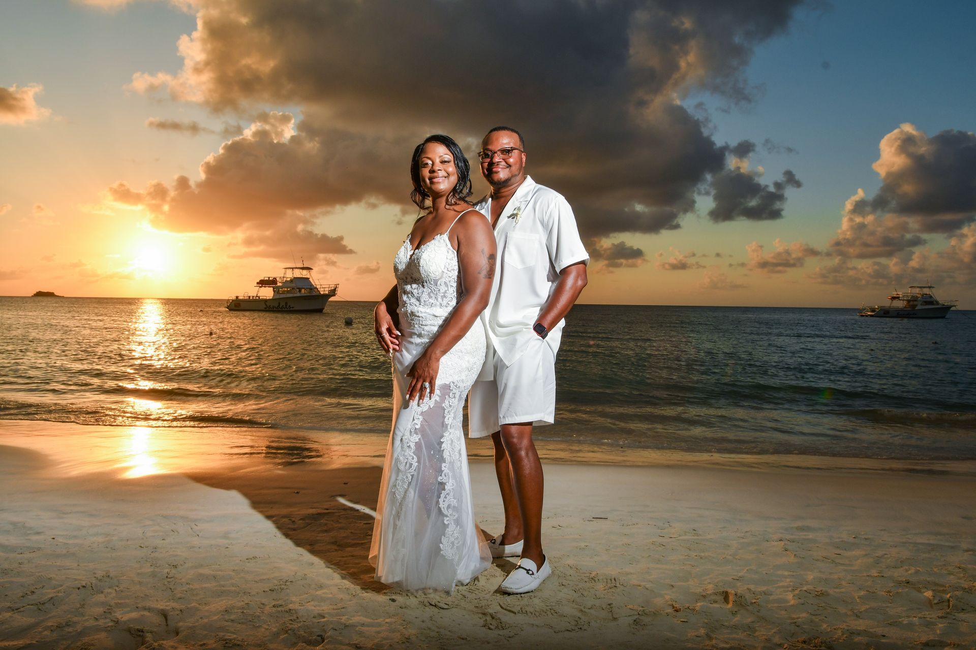 A bride and groom are posing for a picture on the beach at sunset.