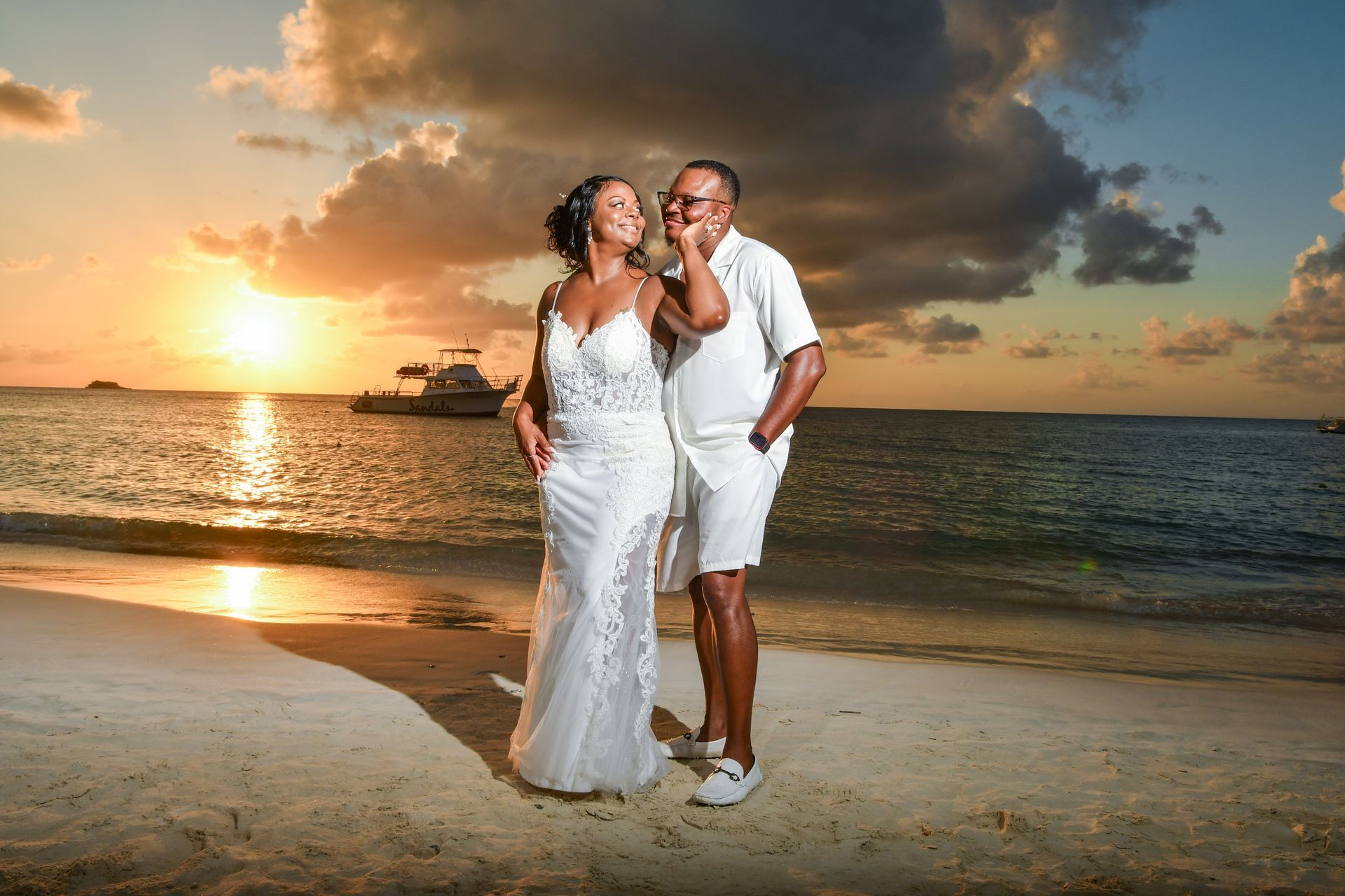 A bride and groom are posing for a picture on the beach at sunset.