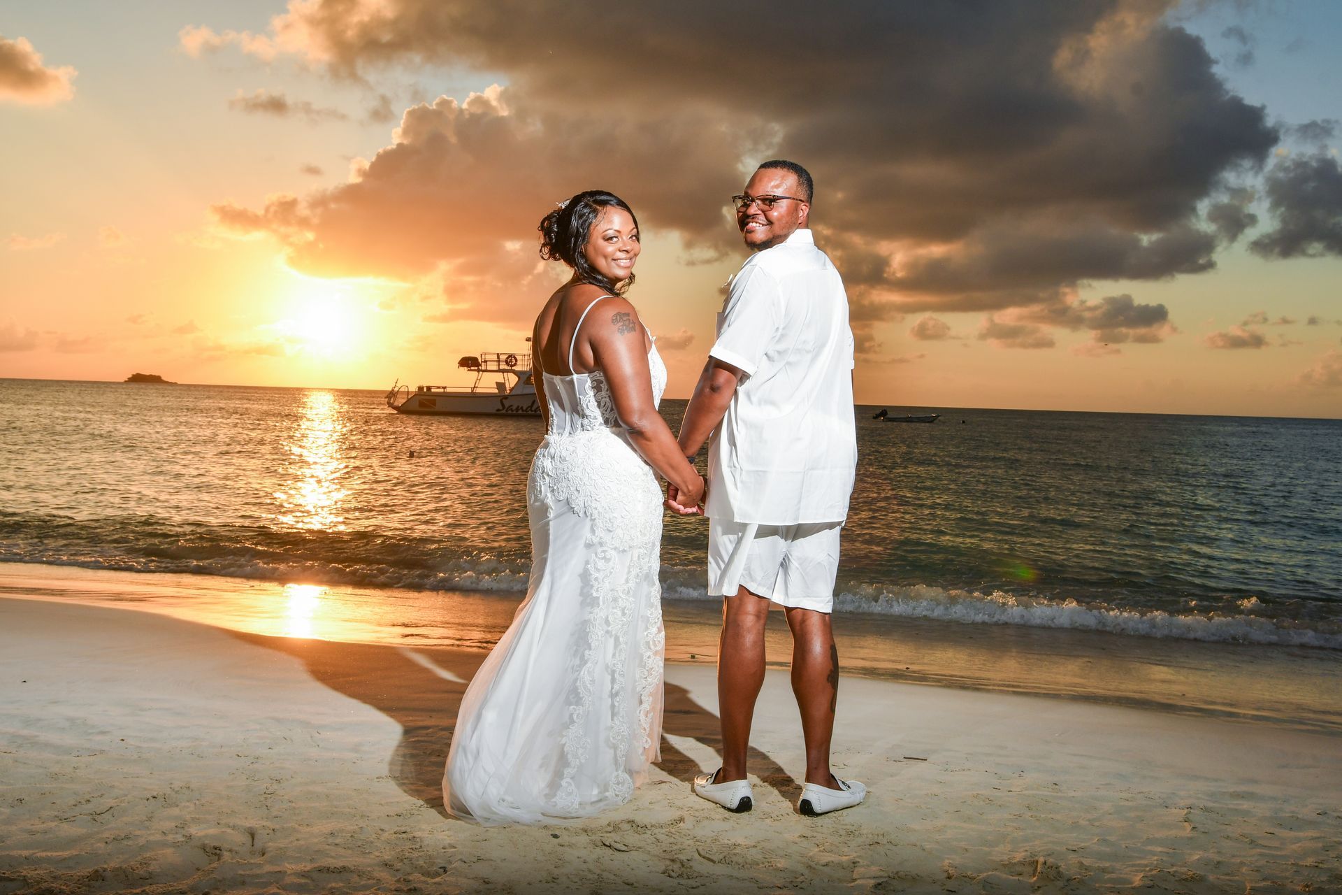 A bride and groom are holding hands on the beach at sunset.