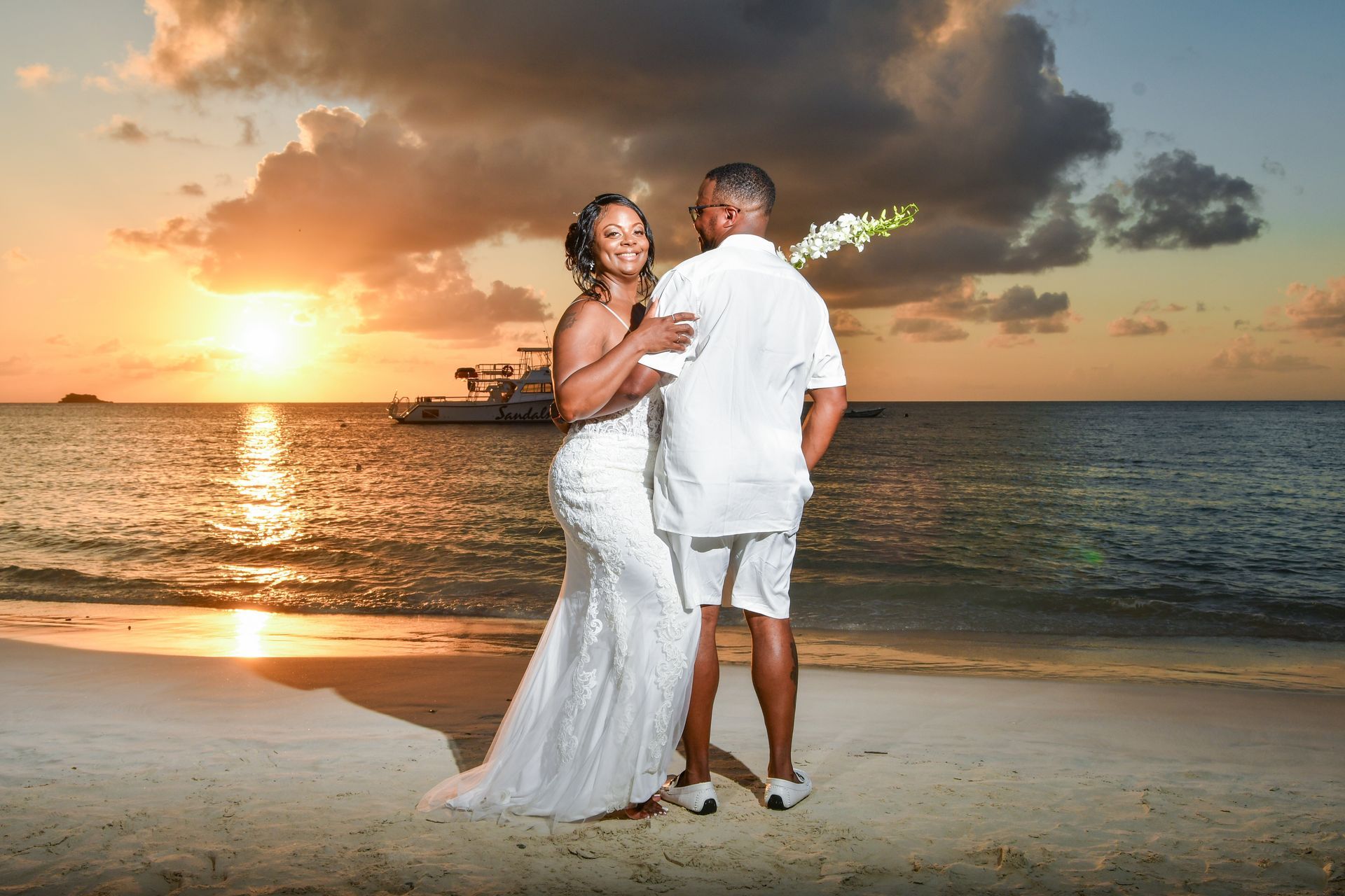 A bride and groom are dancing on the beach at sunset.