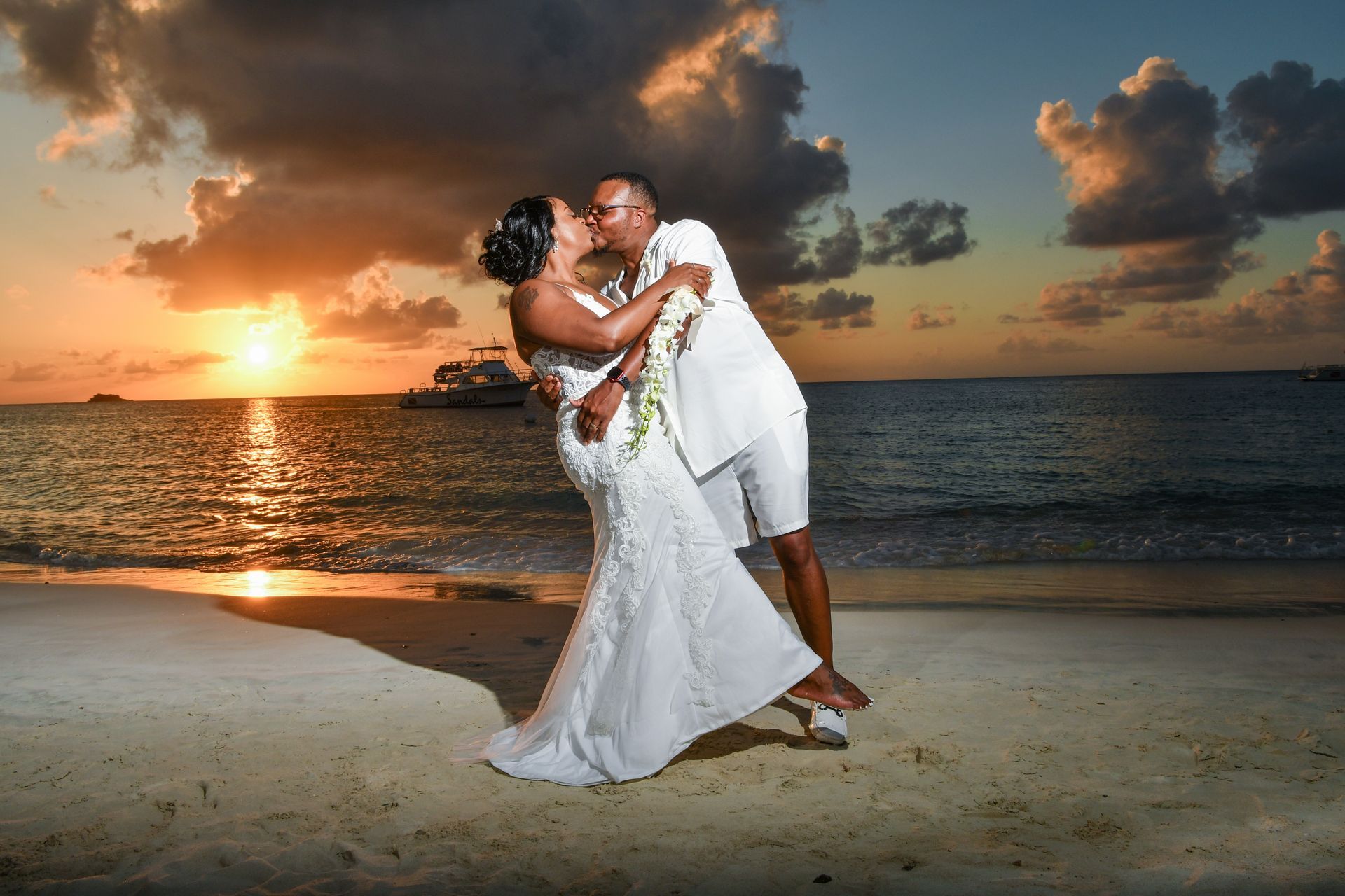 A bride and groom are kissing on the beach at sunset.