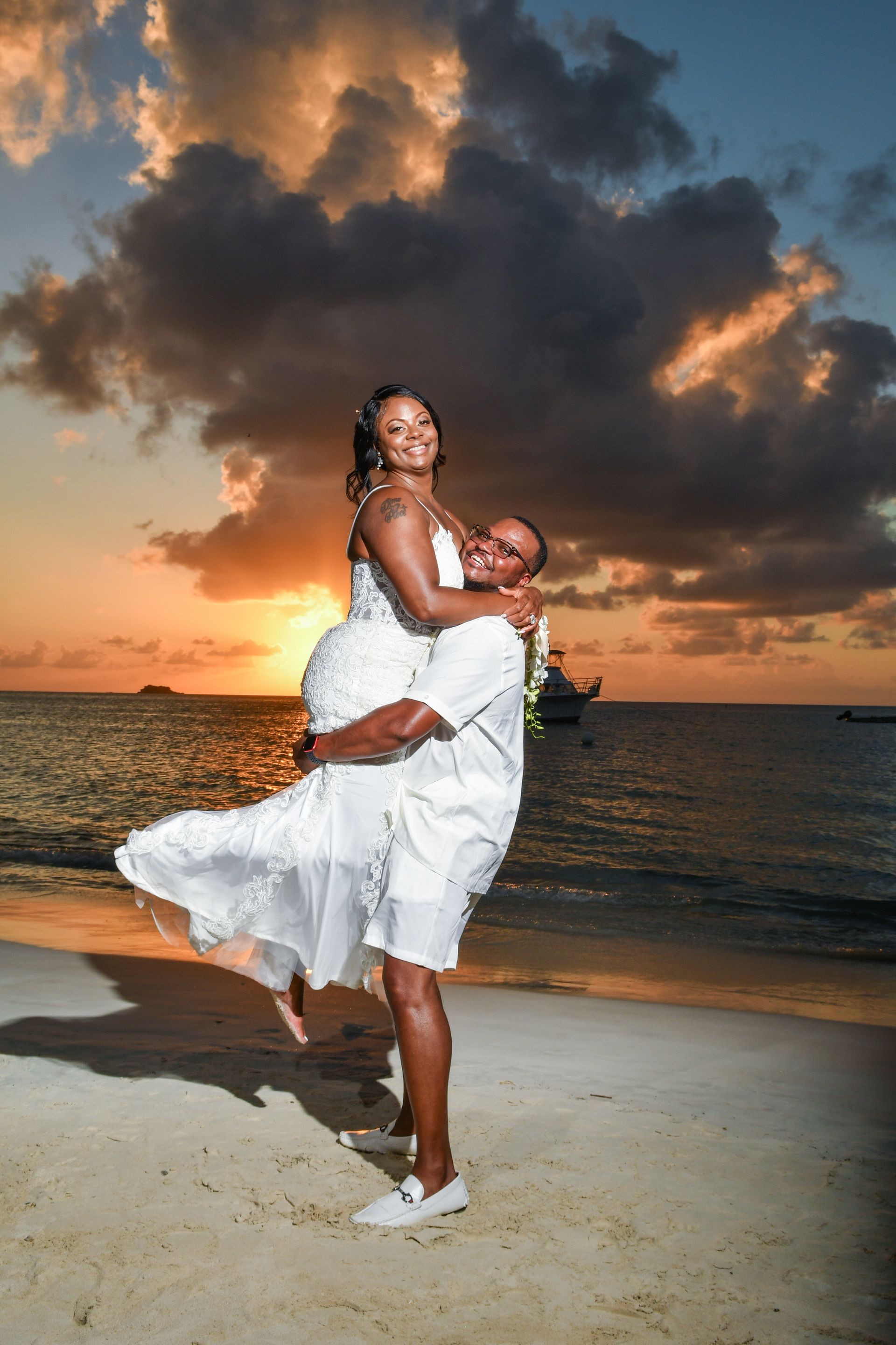 A man is holding a woman in his arms on the beach at sunset.