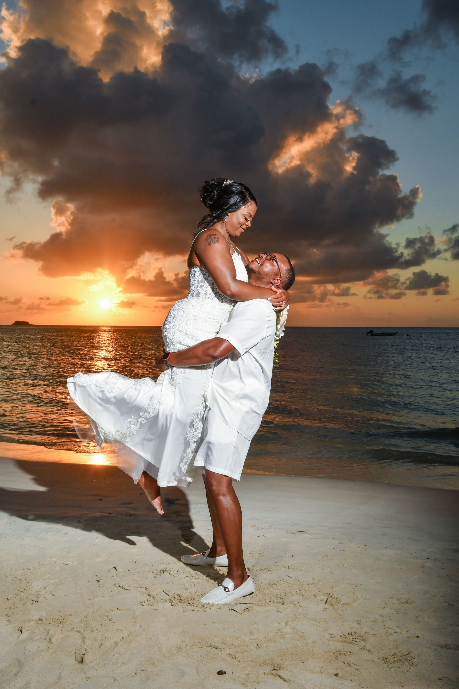 A man is holding a woman in his arms on a beach at sunset.