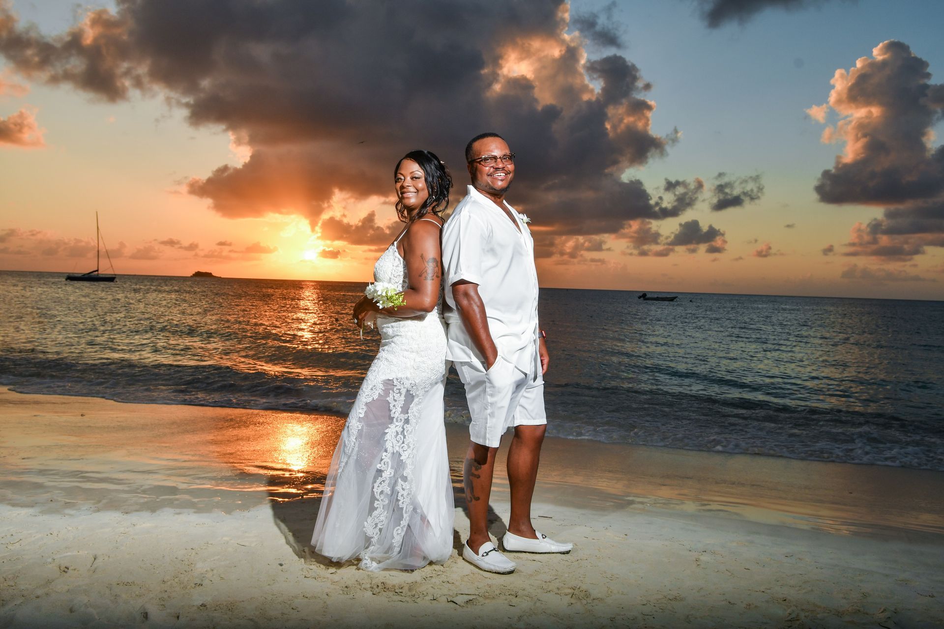 A bride and groom are posing for a picture on the beach at sunset.