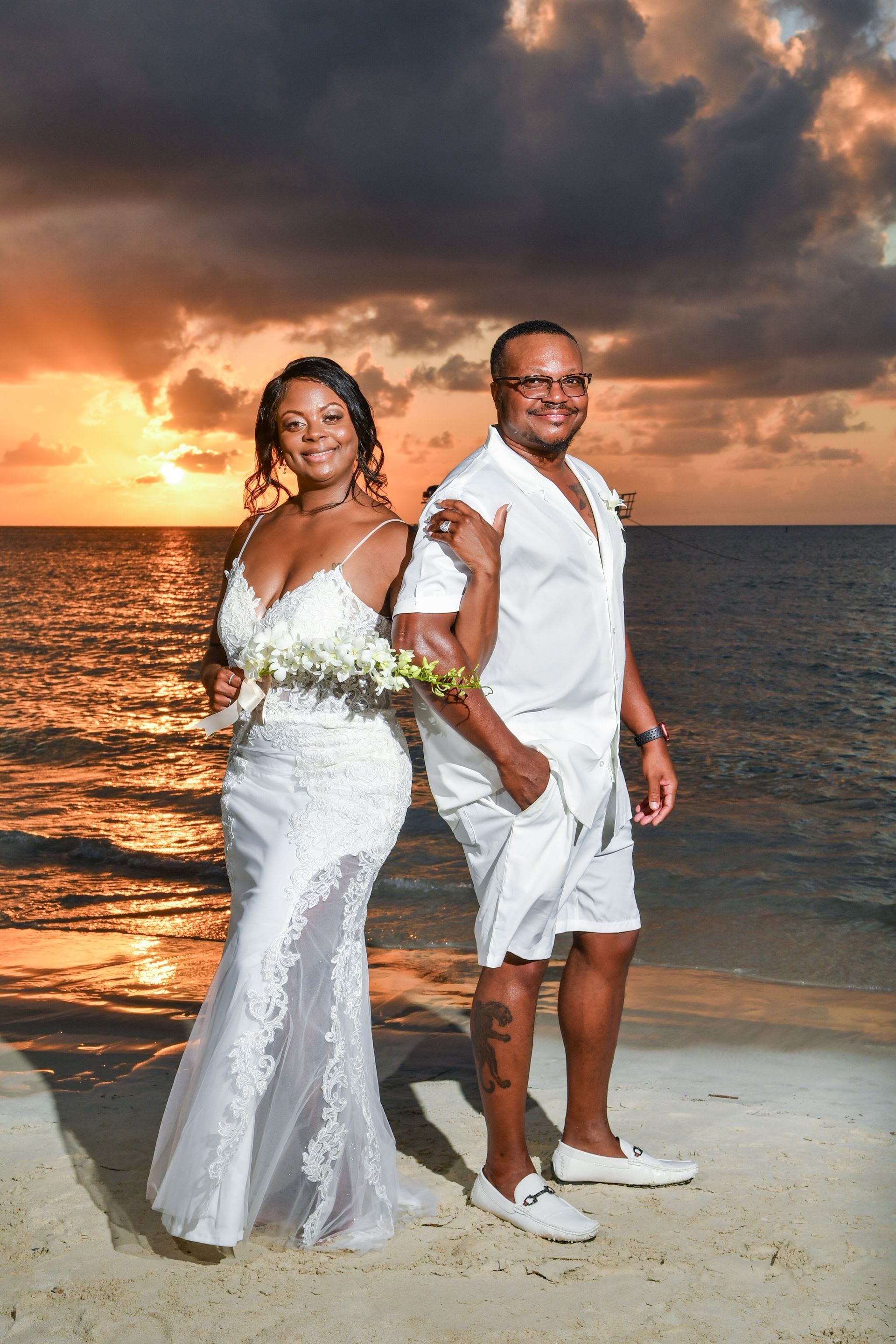 A bride and groom are posing for a picture on the beach at sunset.