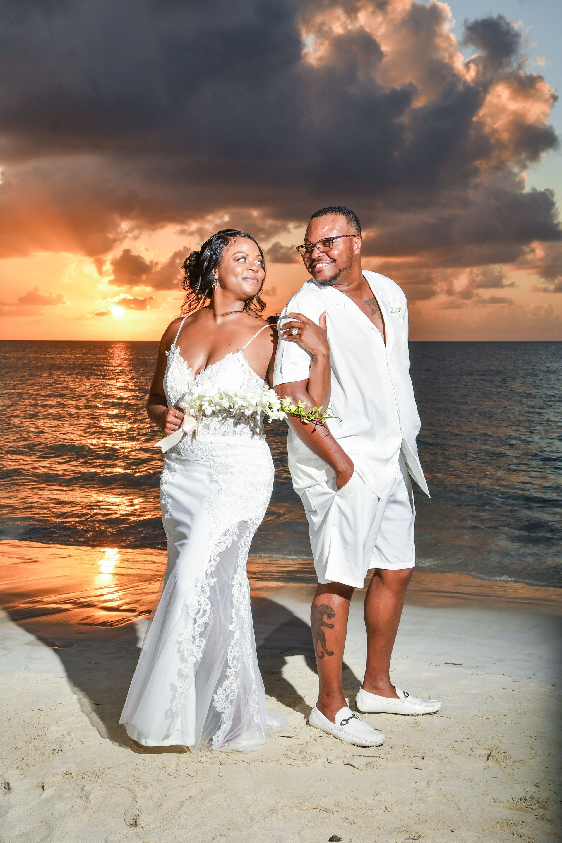 A bride and groom are posing for a picture on the beach at sunset.