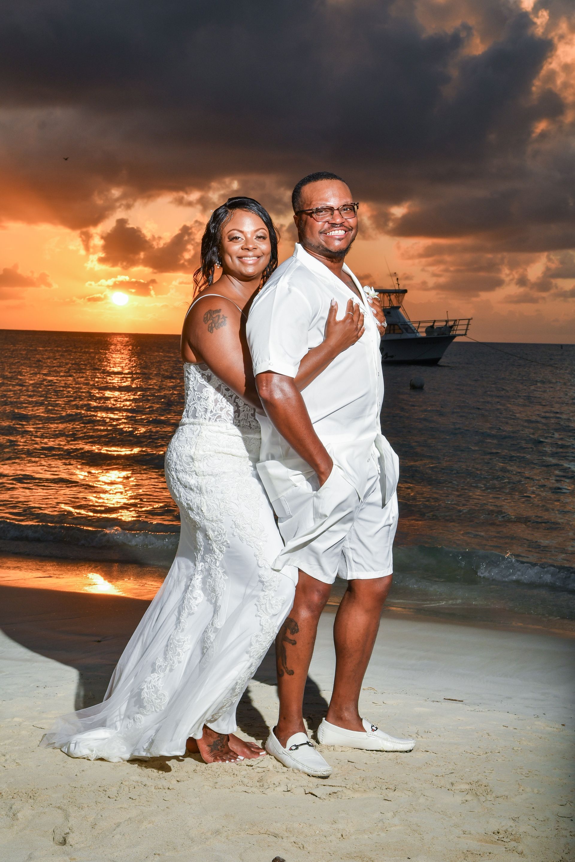 A bride and groom are posing for a picture on the beach at sunset.