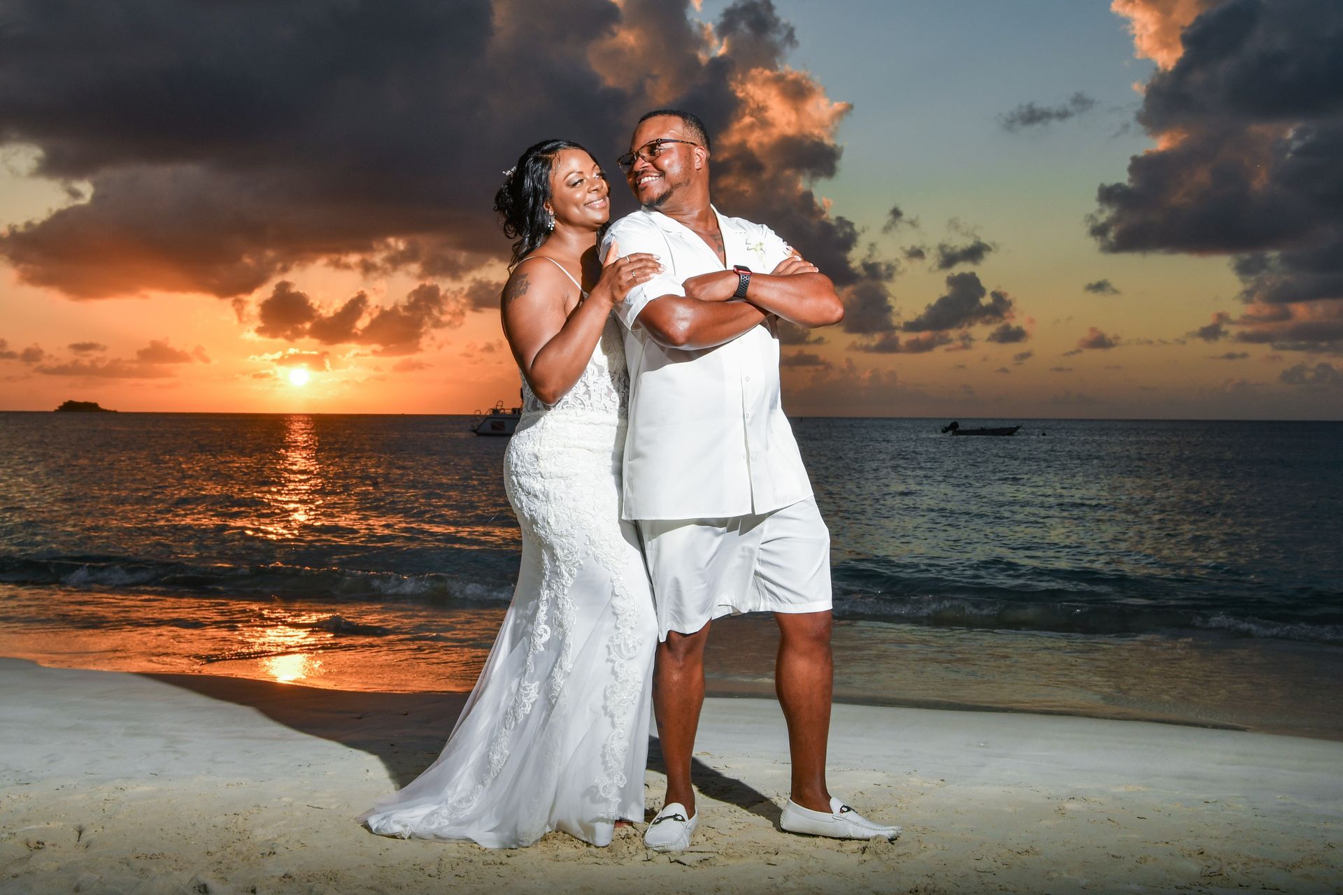 A bride and groom are posing for a picture on the beach at sunset.