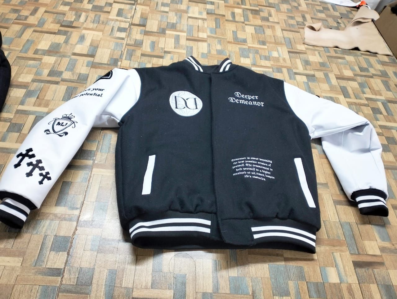 A black and white varsity jacket is laying on a wooden floor