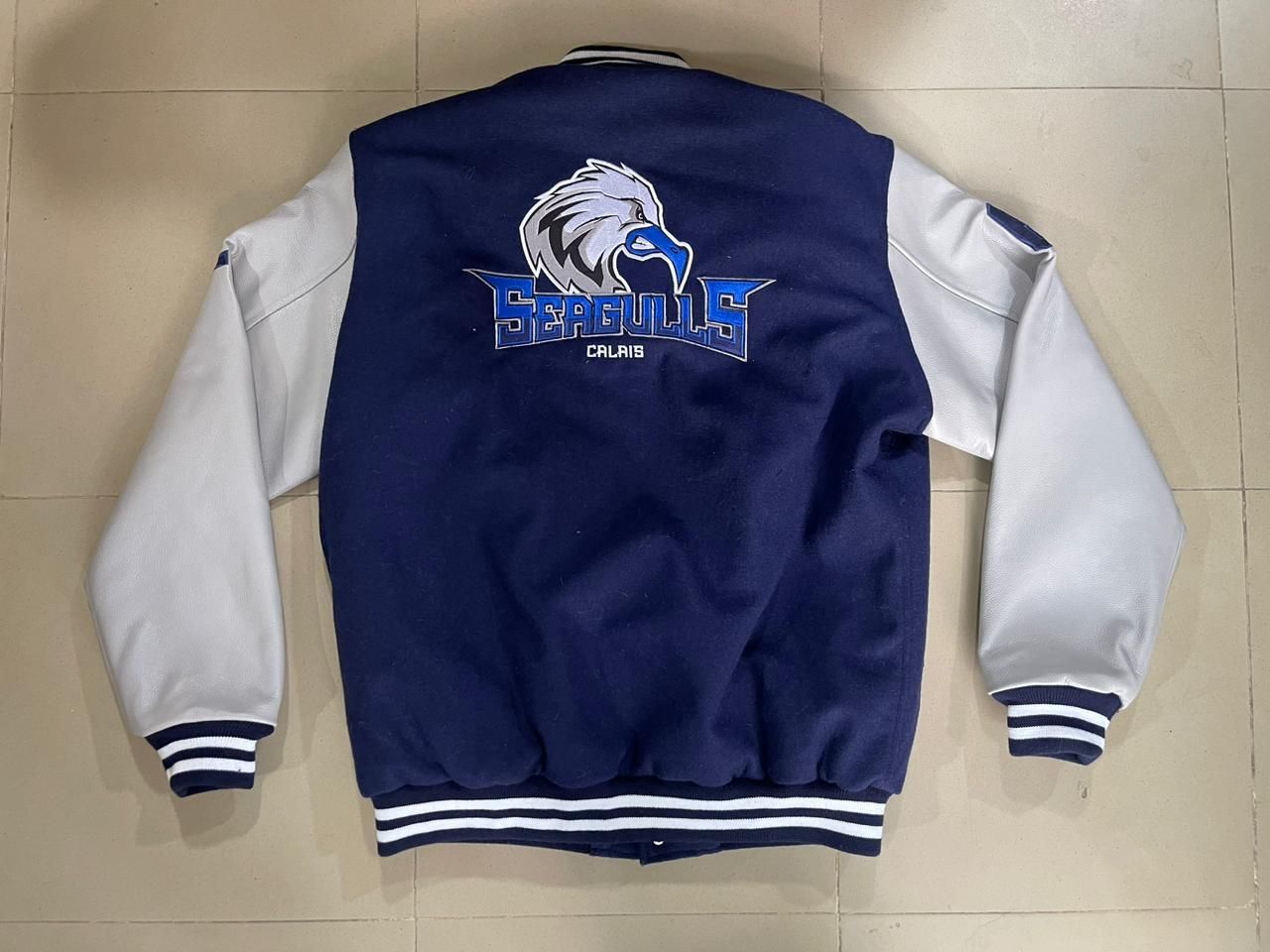 A blue and white baseball jacket with the word seagulls on the back