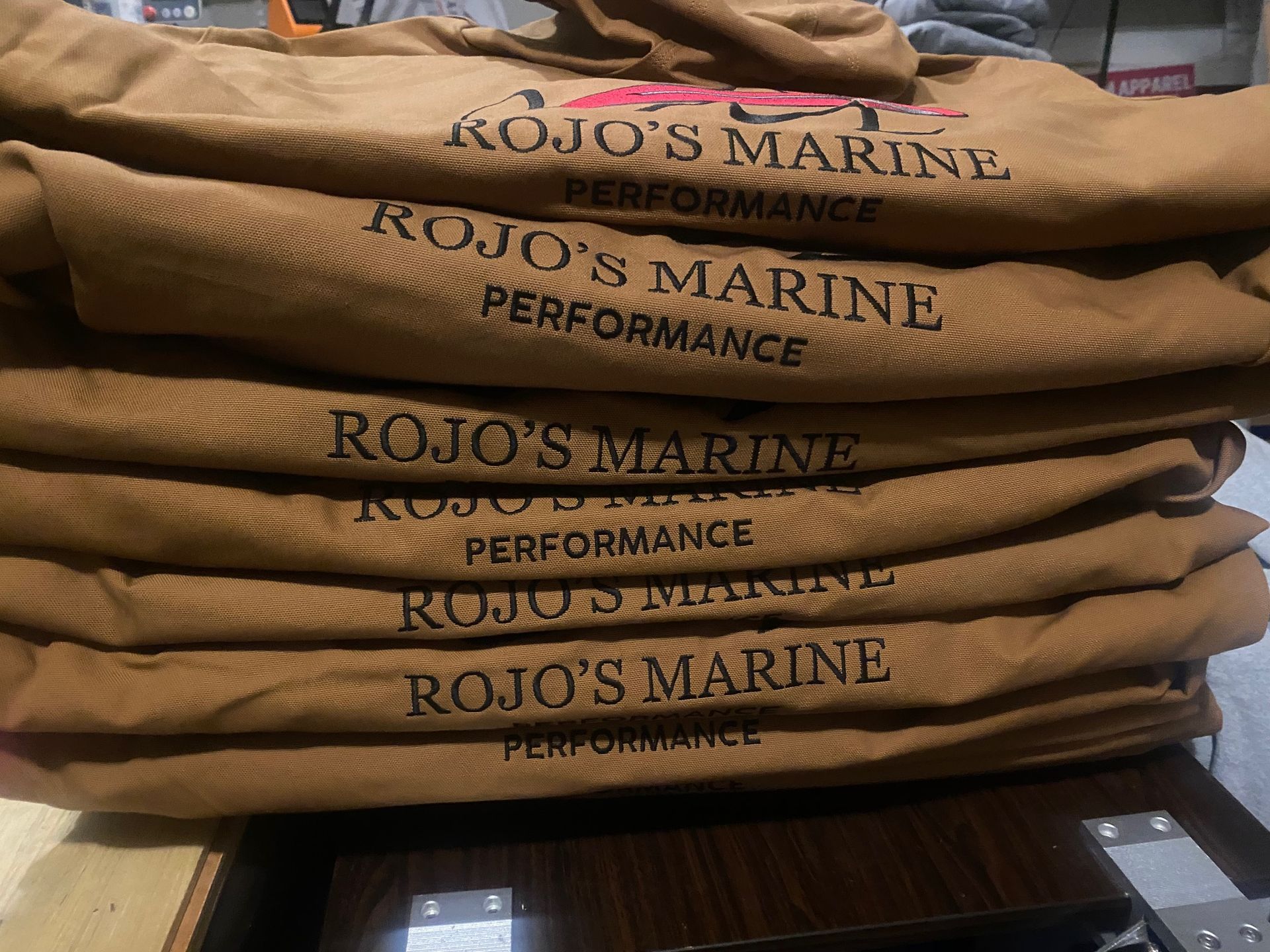 A stack of brown shirts that say rojo 's marine performance