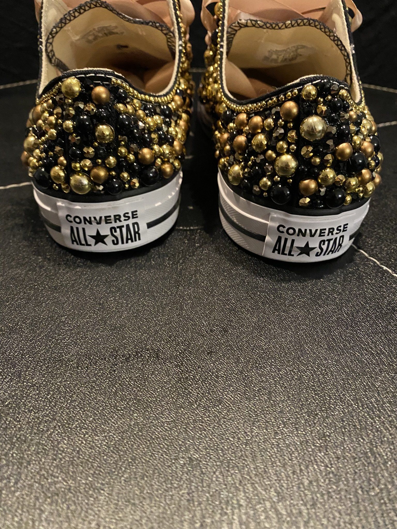 A pair of converse shoes with black and gold beads on them.