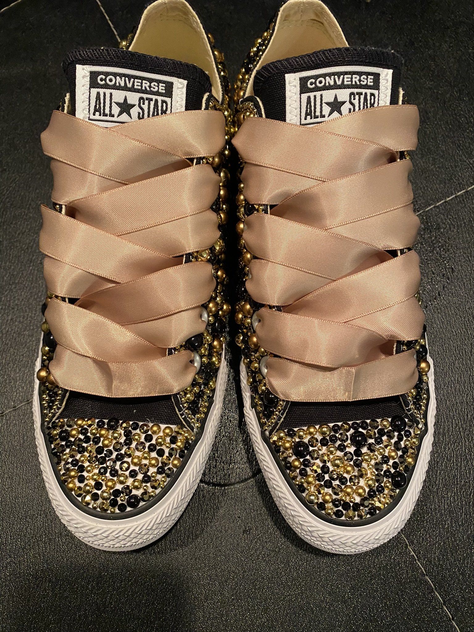 A pair of black and gold converse shoes with ribbon laces.